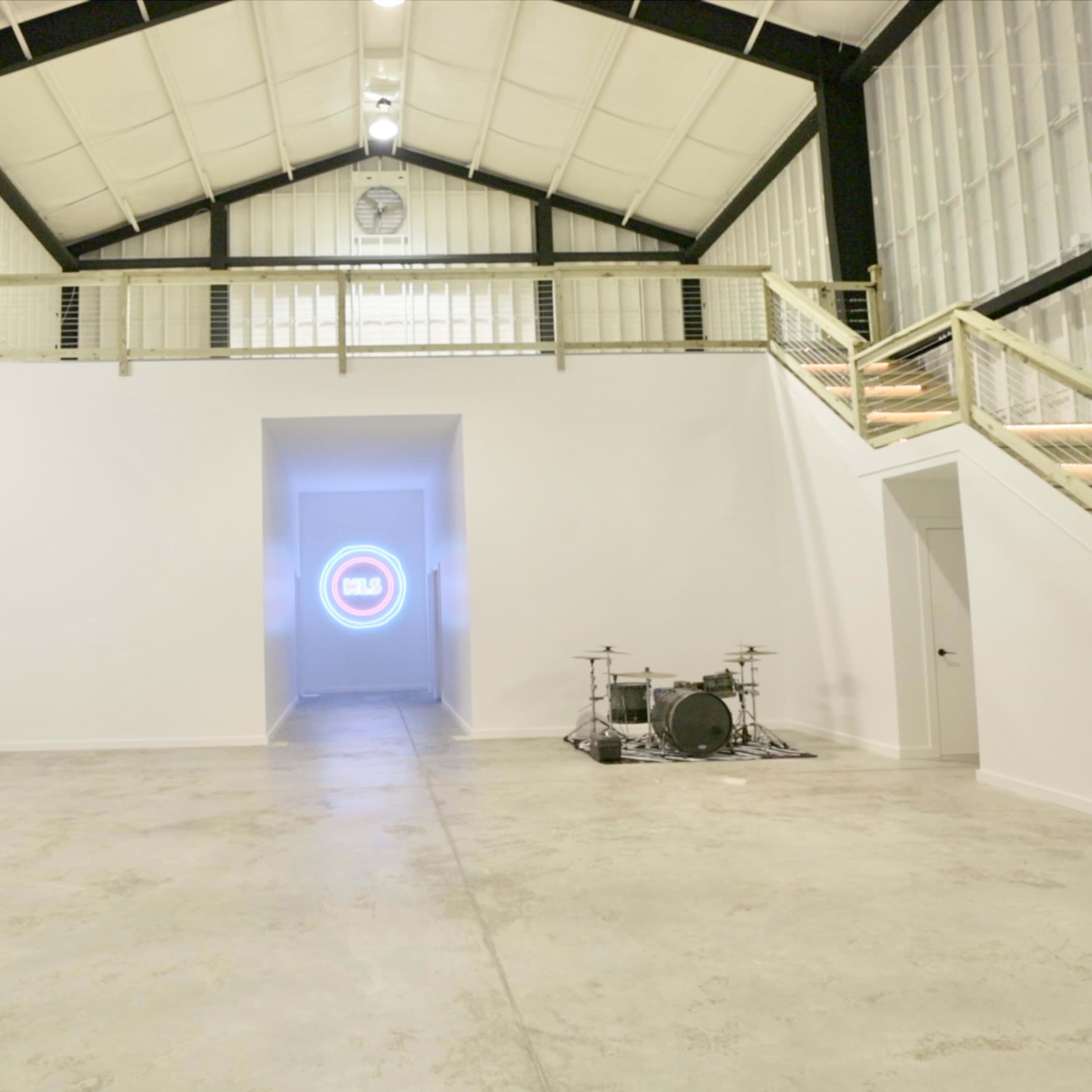 A spacious, empty interior with white walls, a large opening at the far end, and a small drum set positioned to the side.