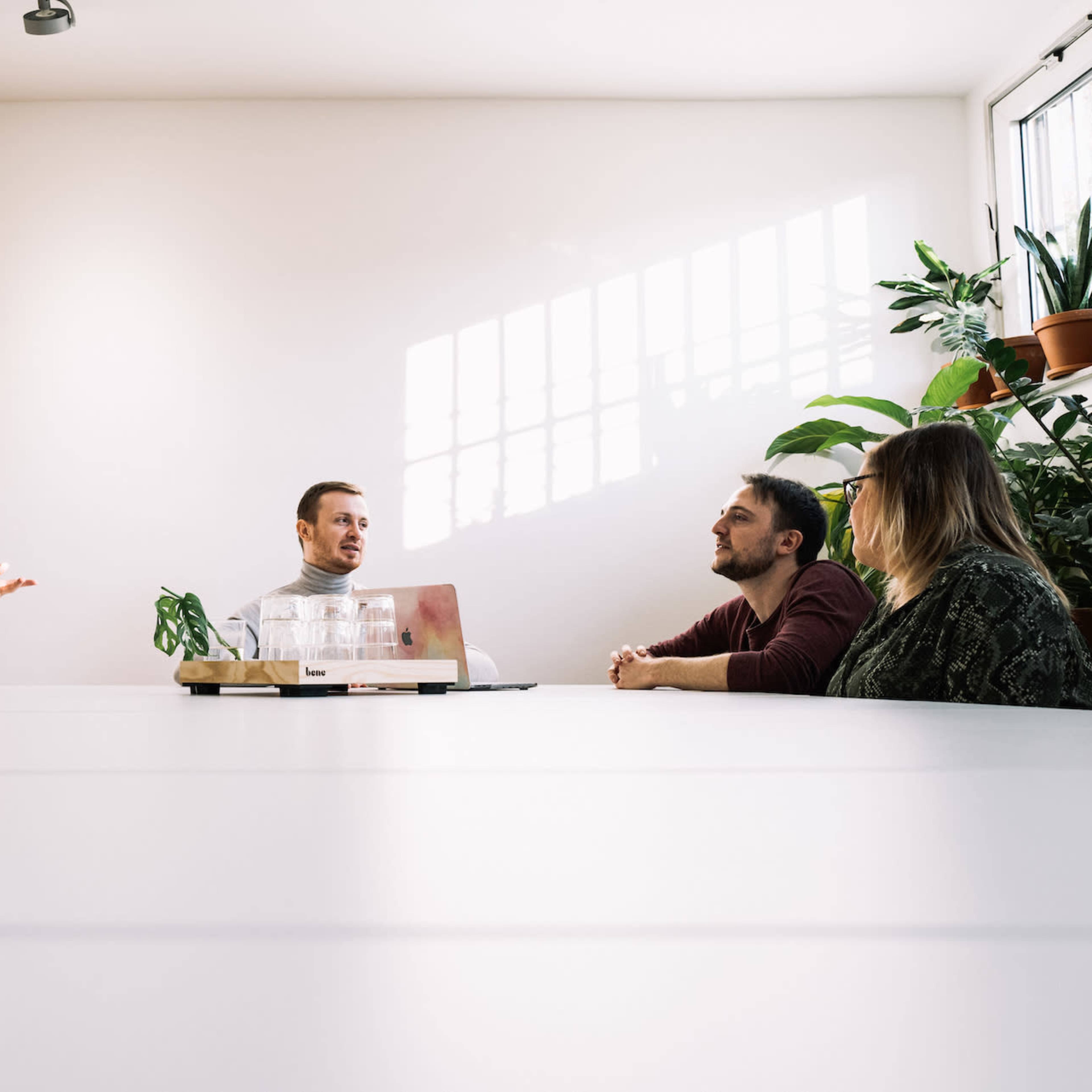 A group of five people are engaged in a discussion around a large table in a well-lit office space.