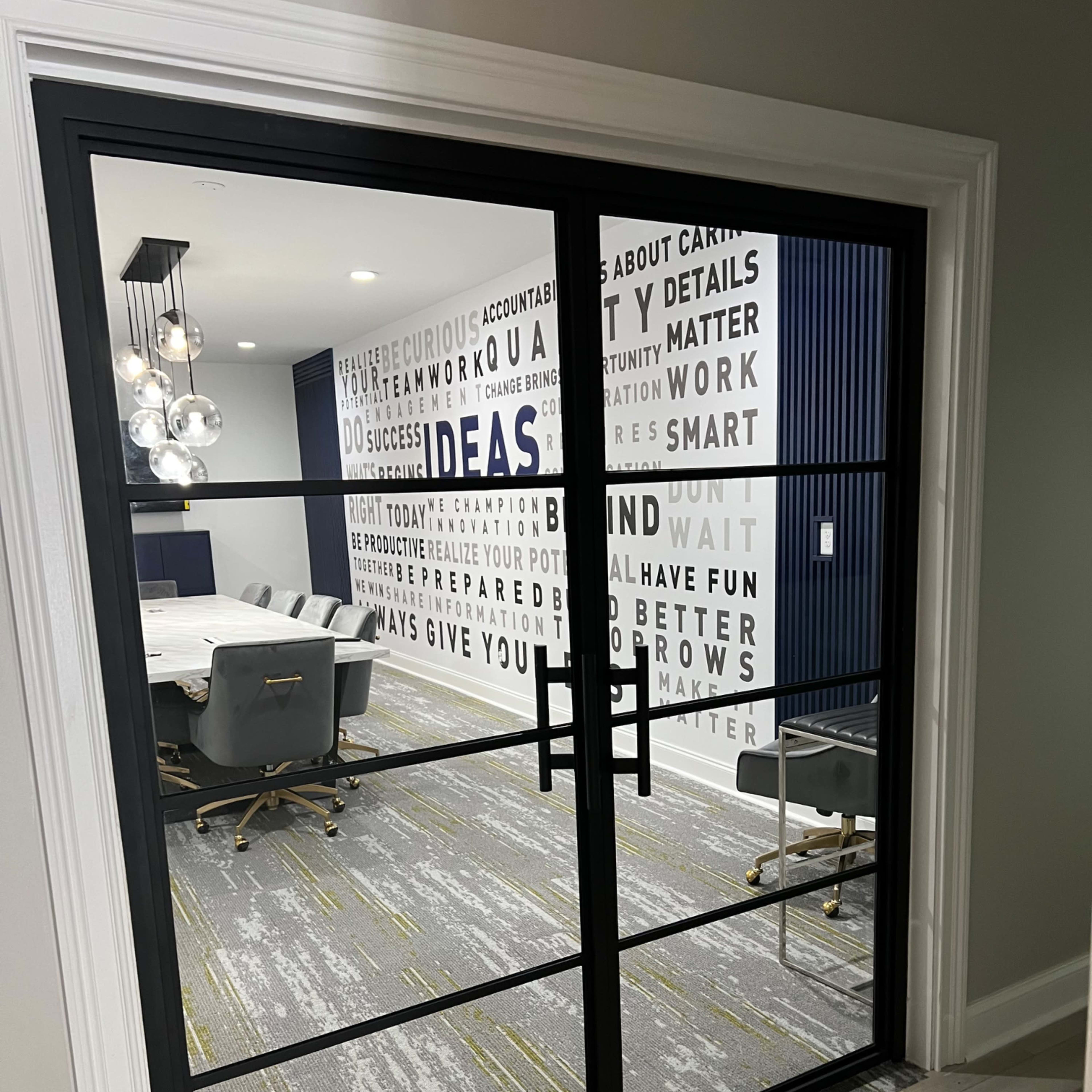 A modern conference room with a large table and chairs, featuring a wall adorned with motivational words and phrases.