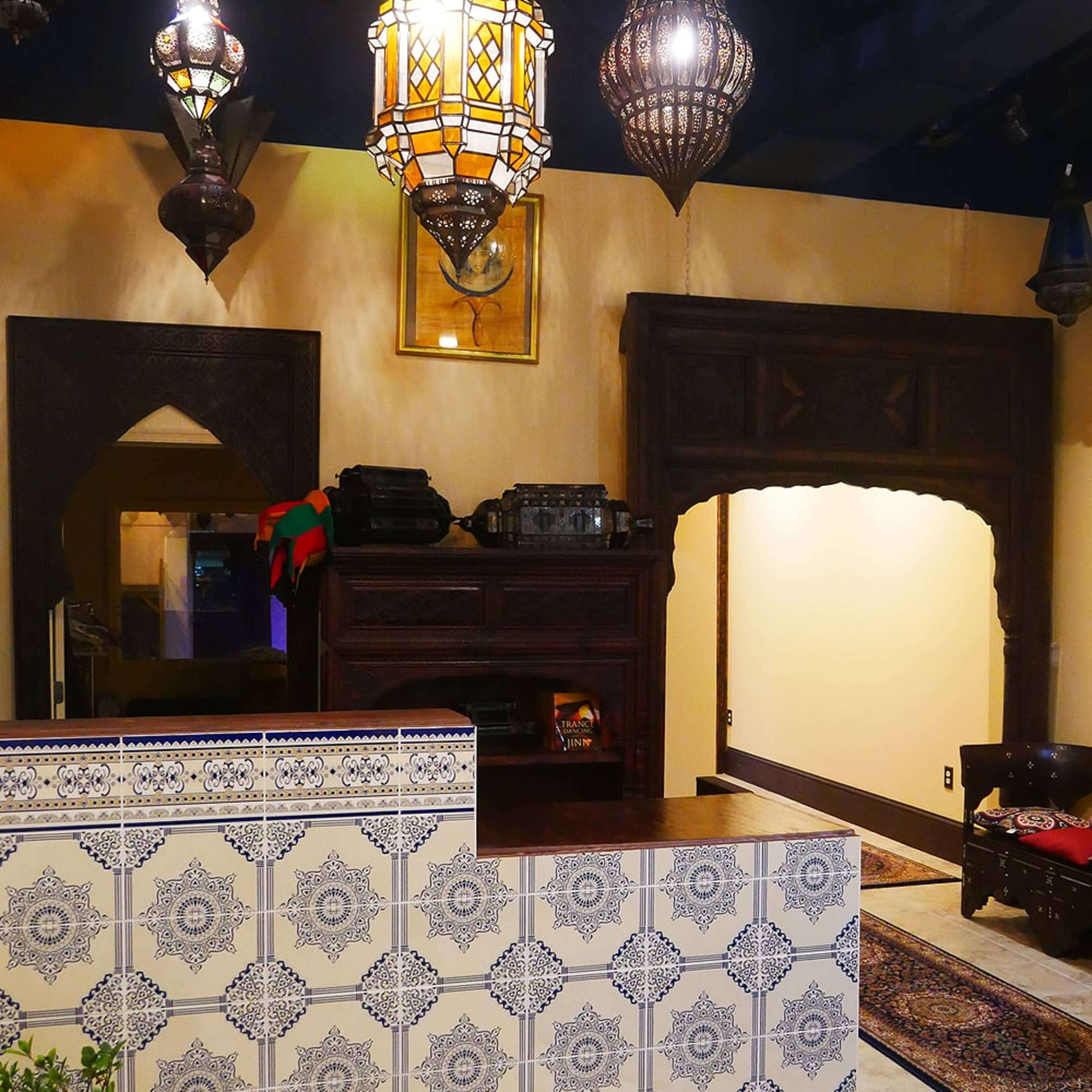 The interior of a Moroccan-style reception area features ornate light fixtures, intricate tile work, and an arched doorway leading to another room.