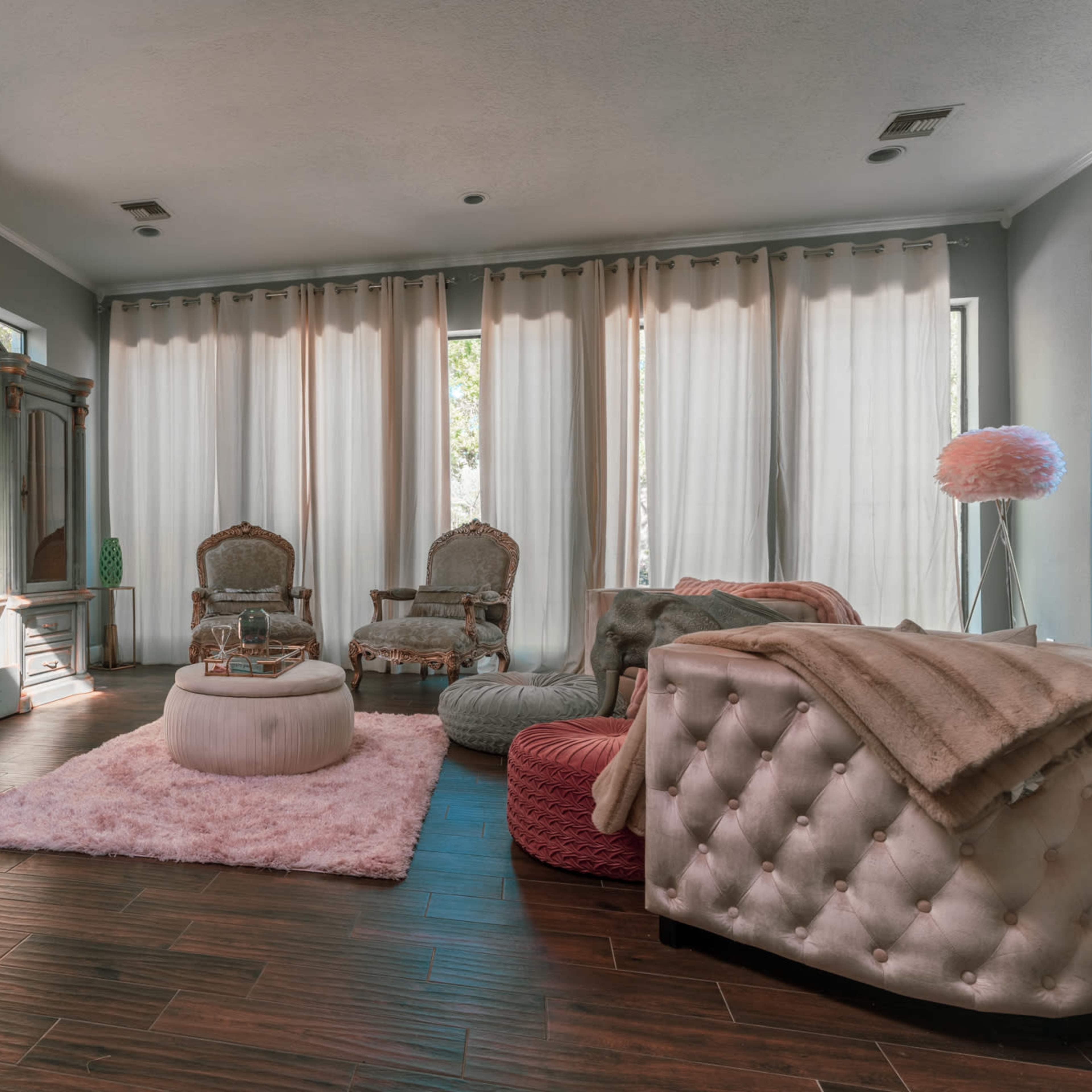 The room features elegant furniture, soft textiles, large windows with sheer curtains, and a cozy arrangement of seating areas.
