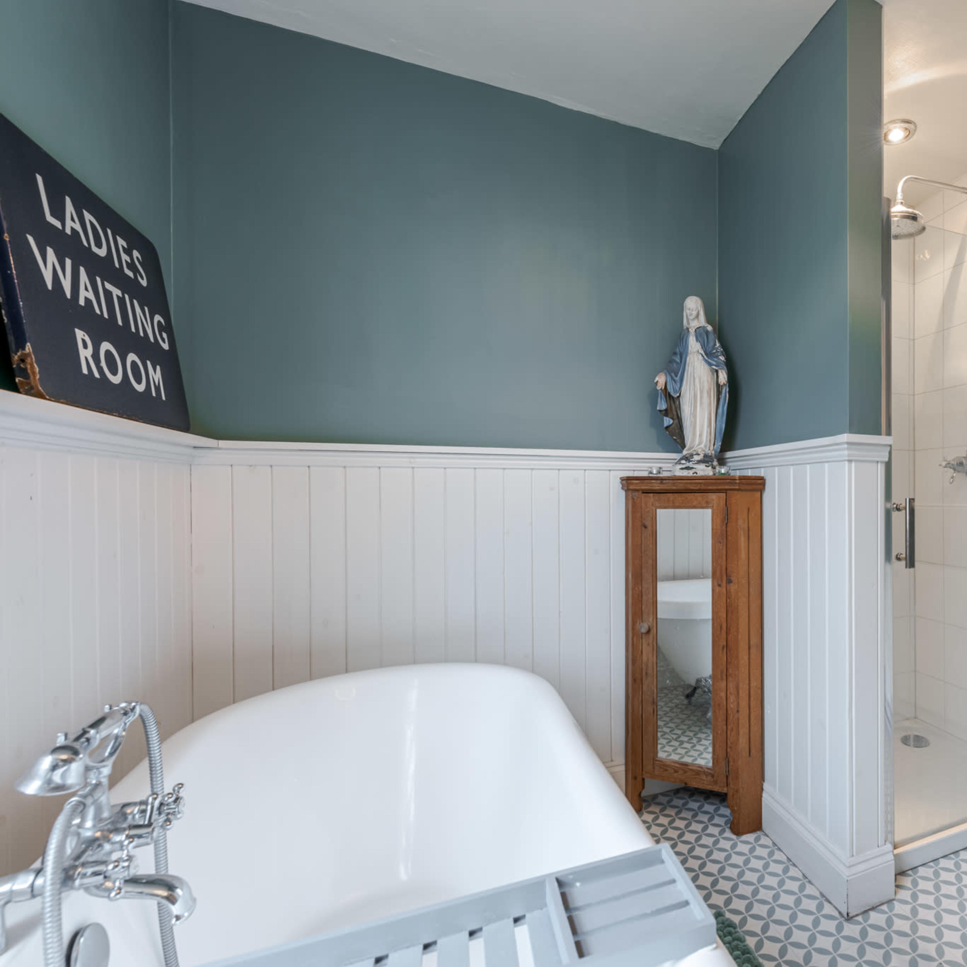 A bathroom with a white bathtub, a walk-in shower, a wooden cabinet, and a framed picture on the wall, all set against a dark green background.