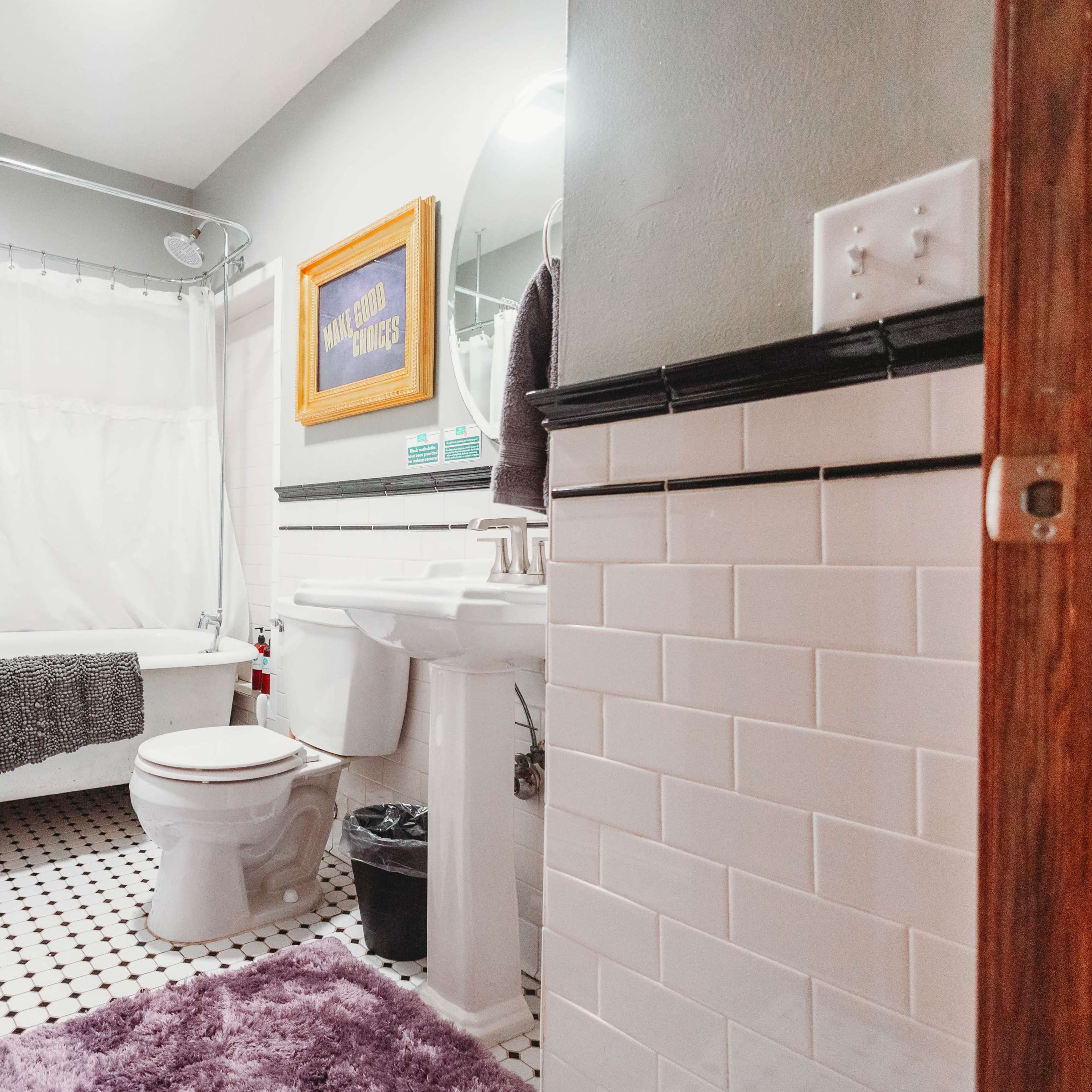 A clean bathroom features a white shower curtain, a bathtub, a toilet, and a sink with tiled walls and black accents.
