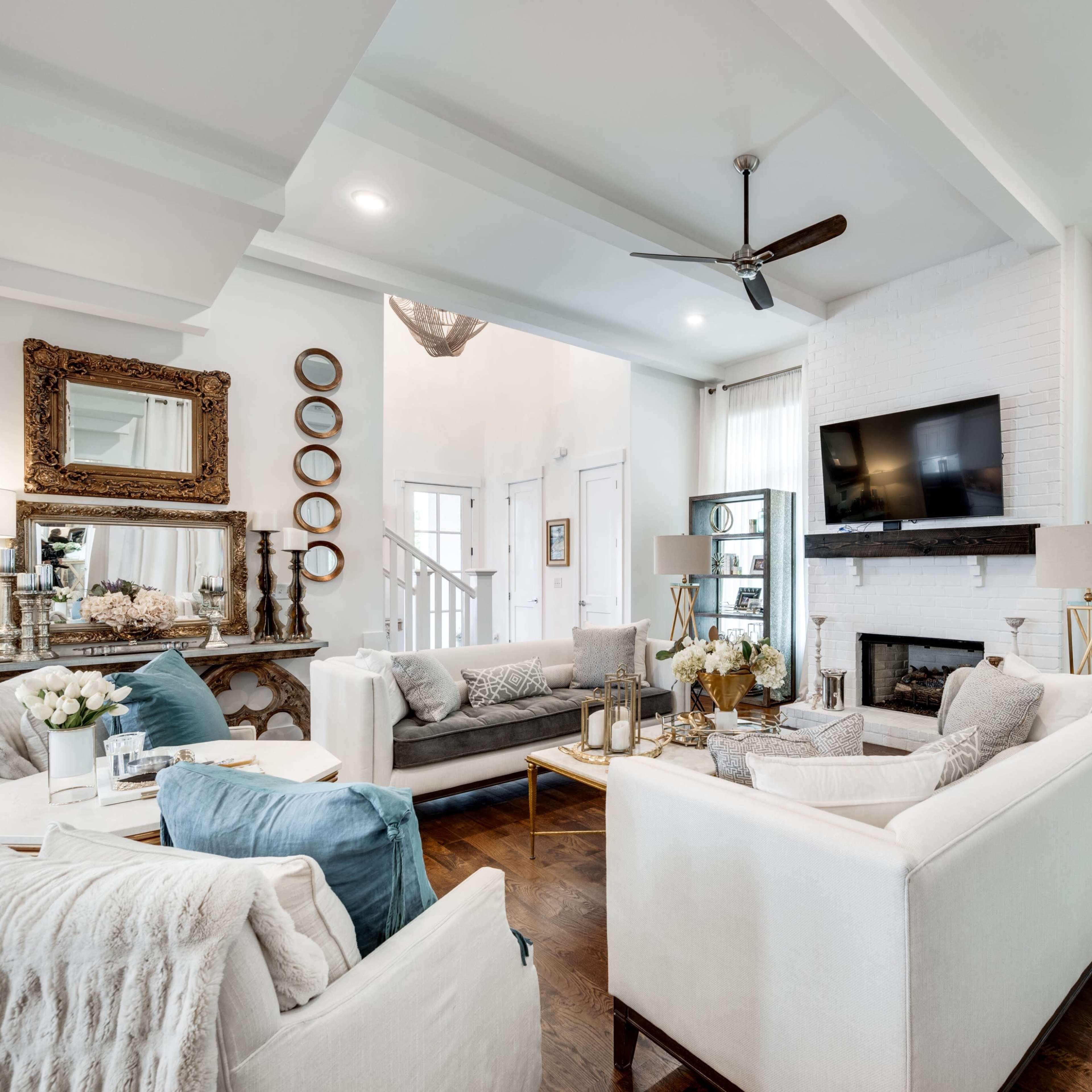 A bright and modern living room with light-colored sofas, a television mounted on the wall, and decorative shelves displaying various items.