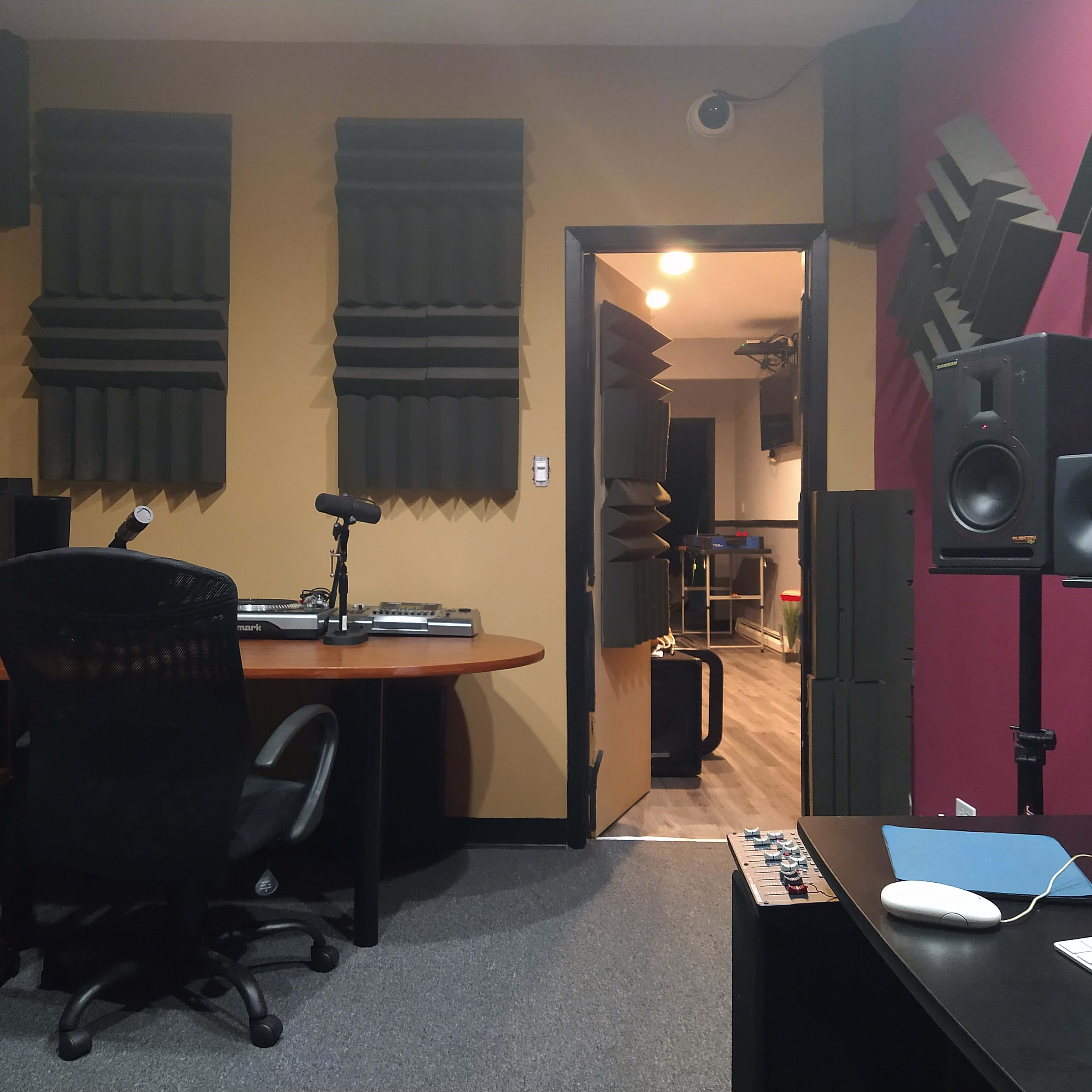 A soundproof recording studio featuring acoustic panels on the walls, a desk with audio equipment, and a doorway leading to another room.
