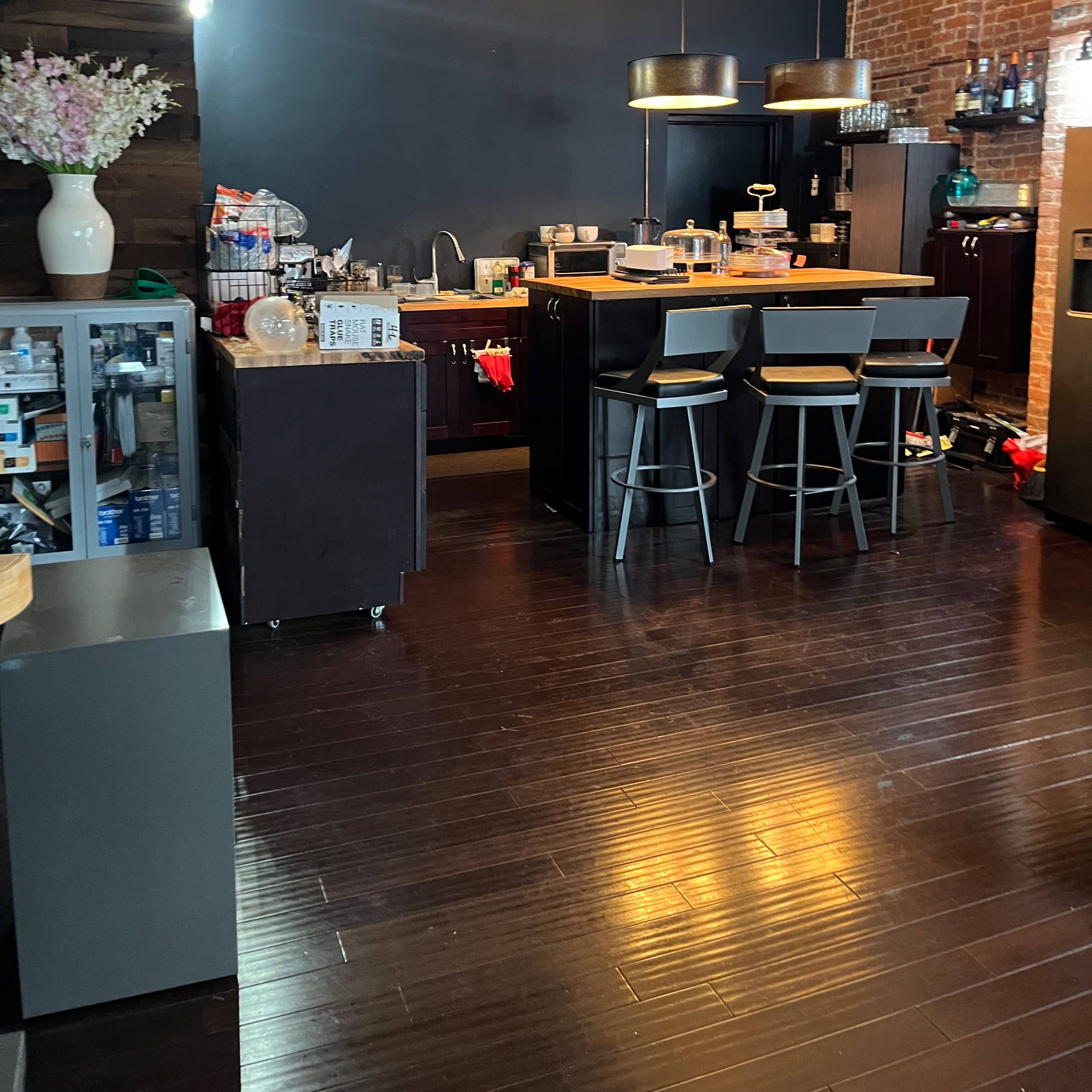 A modern kitchen with dark cabinetry, a central island with bar stools, and exposed brick walls.