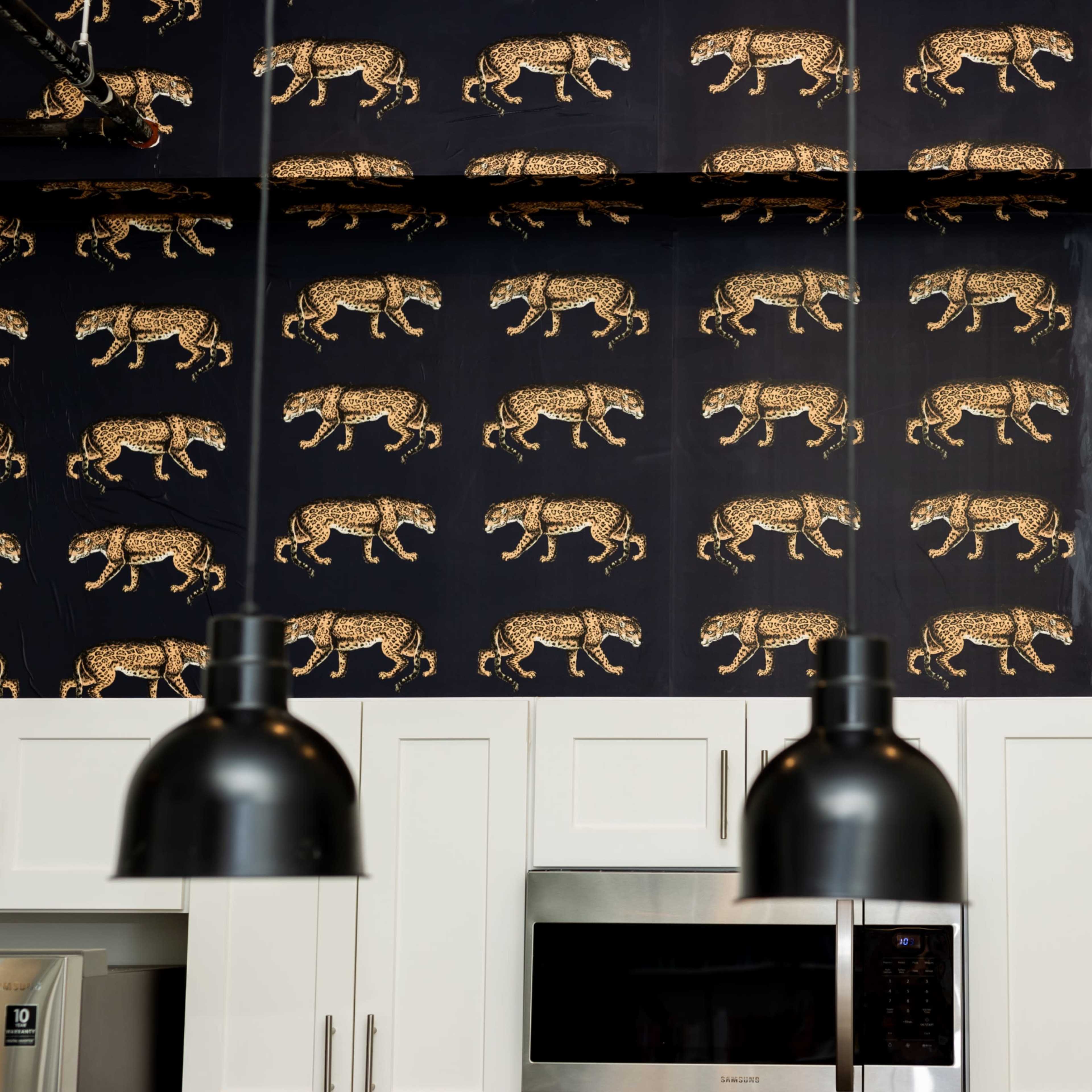 A kitchen with a patterned wallpaper depicting leopards and black pendant lights hanging above white cabinetry.