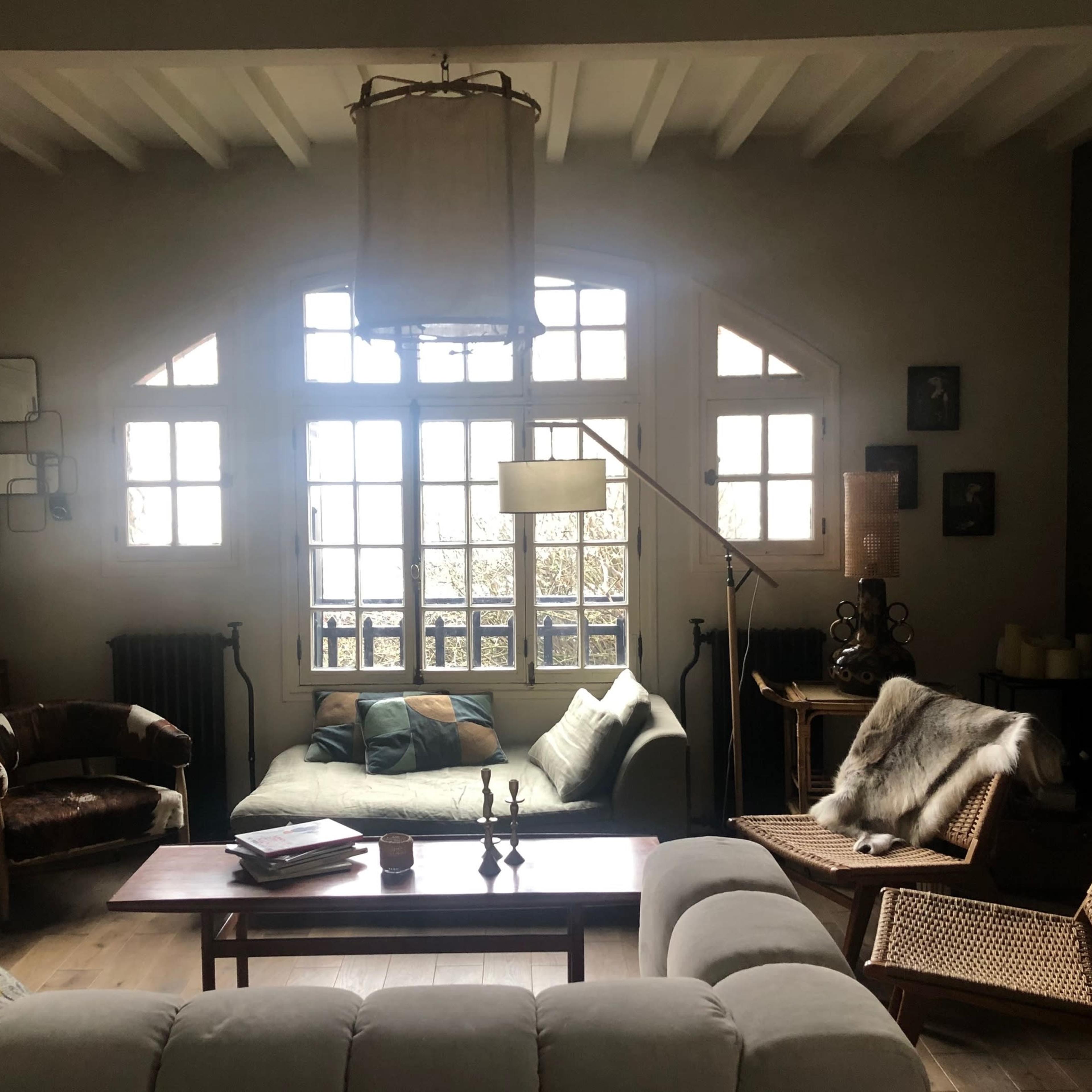 A cozy living room features a mix of seating, large windows, and a wooden coffee table.