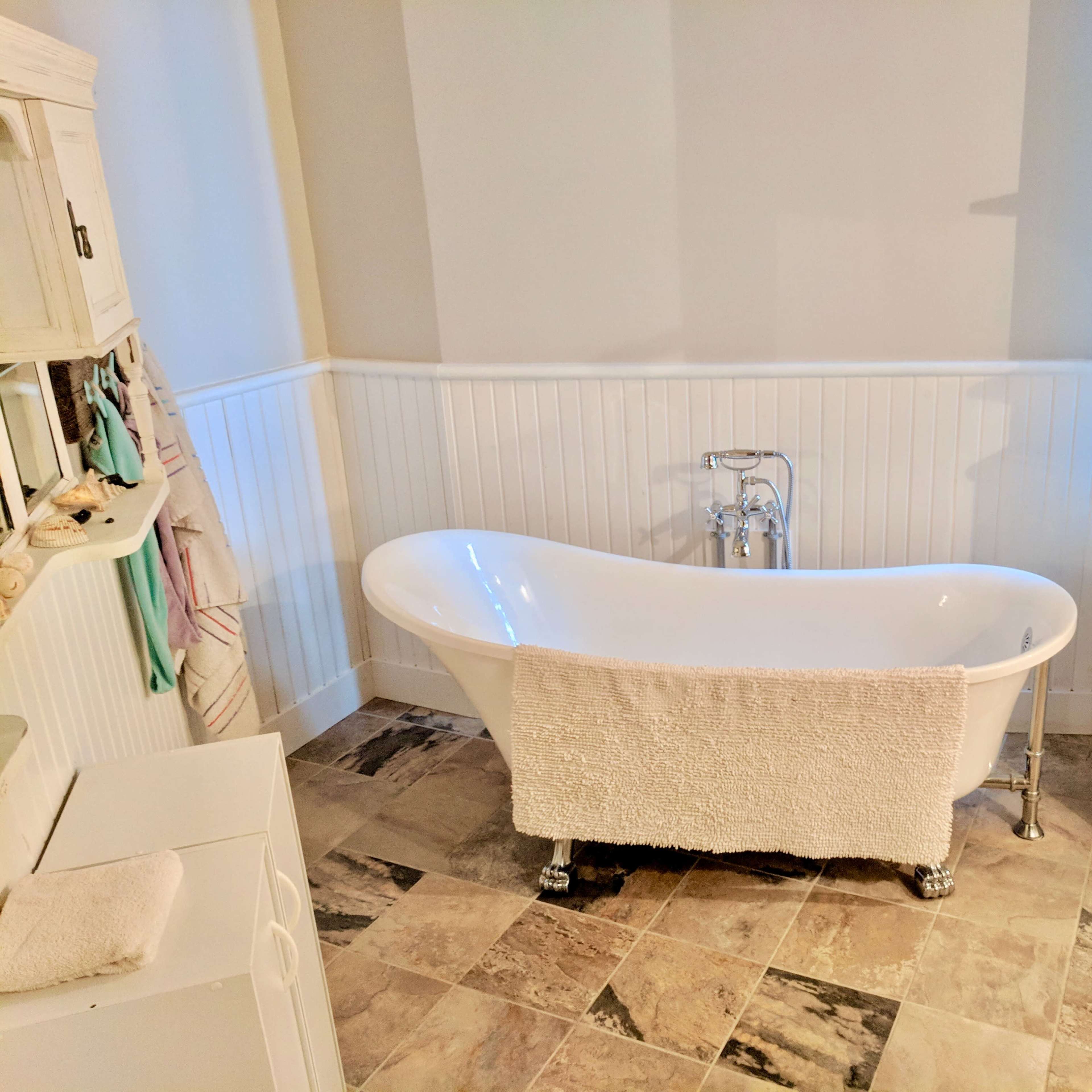 A freestanding white bathtub with a towel draped over it, set against a paneled wall in a bathroom with tiled flooring.
