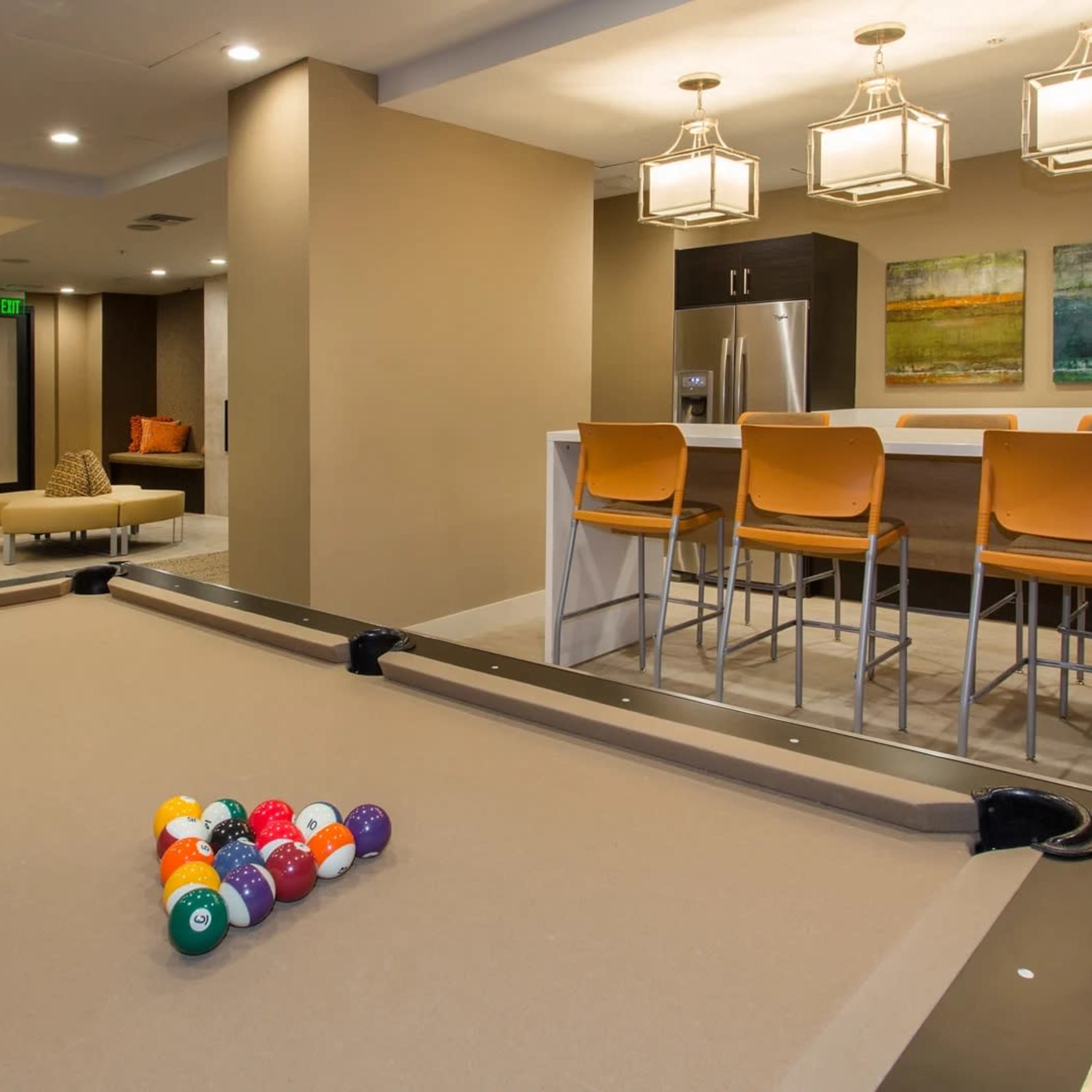 A recreational room featuring a pool table with a set of billiard balls and a bar area with seating and artwork on the wall.