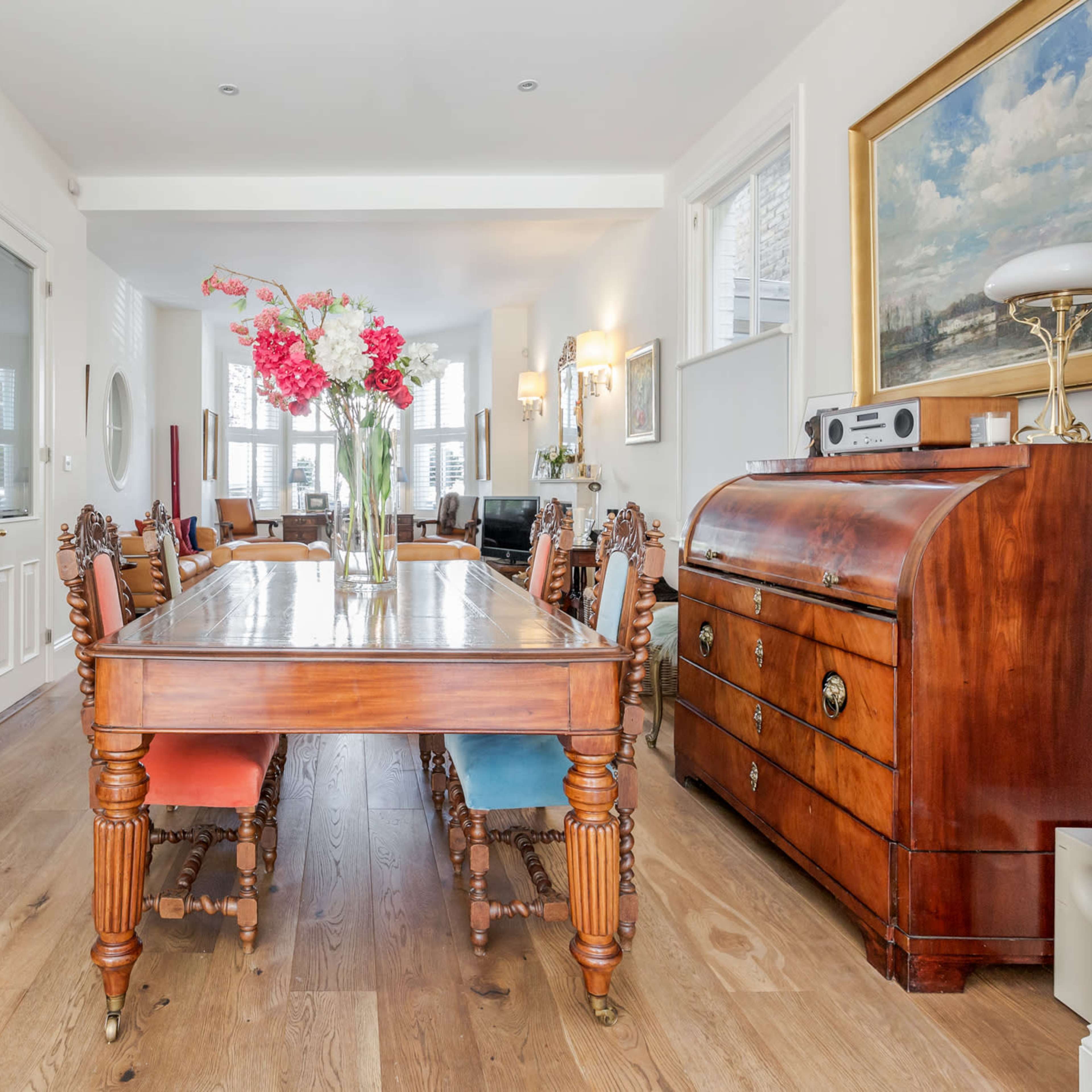 A spacious dining area with a wooden table, chairs with colored upholstery, and decorative furniture pieces along the walls.