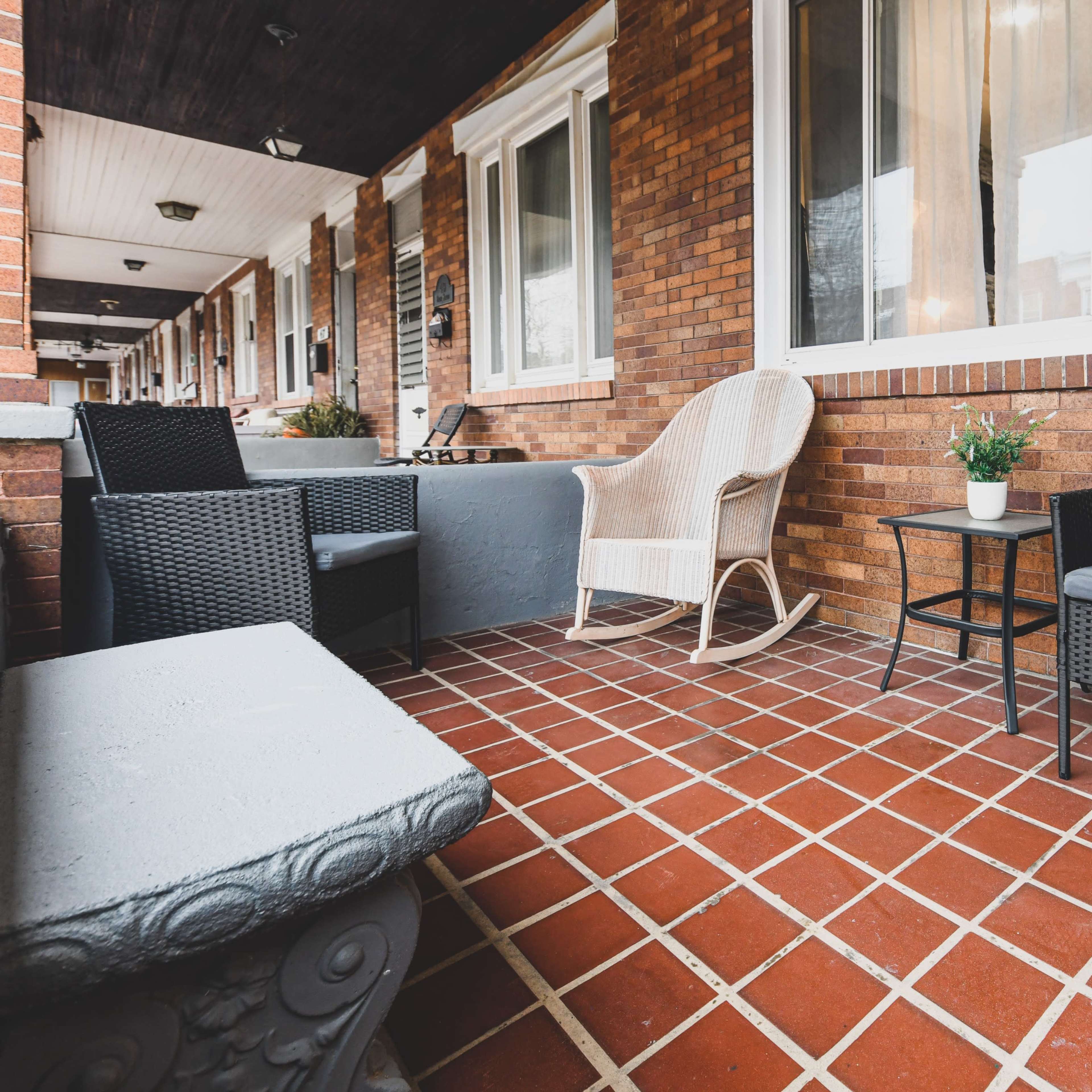 A porch area featuring four chairs, including a rocking chair, a small table, and a potted plant on a tiled floor.