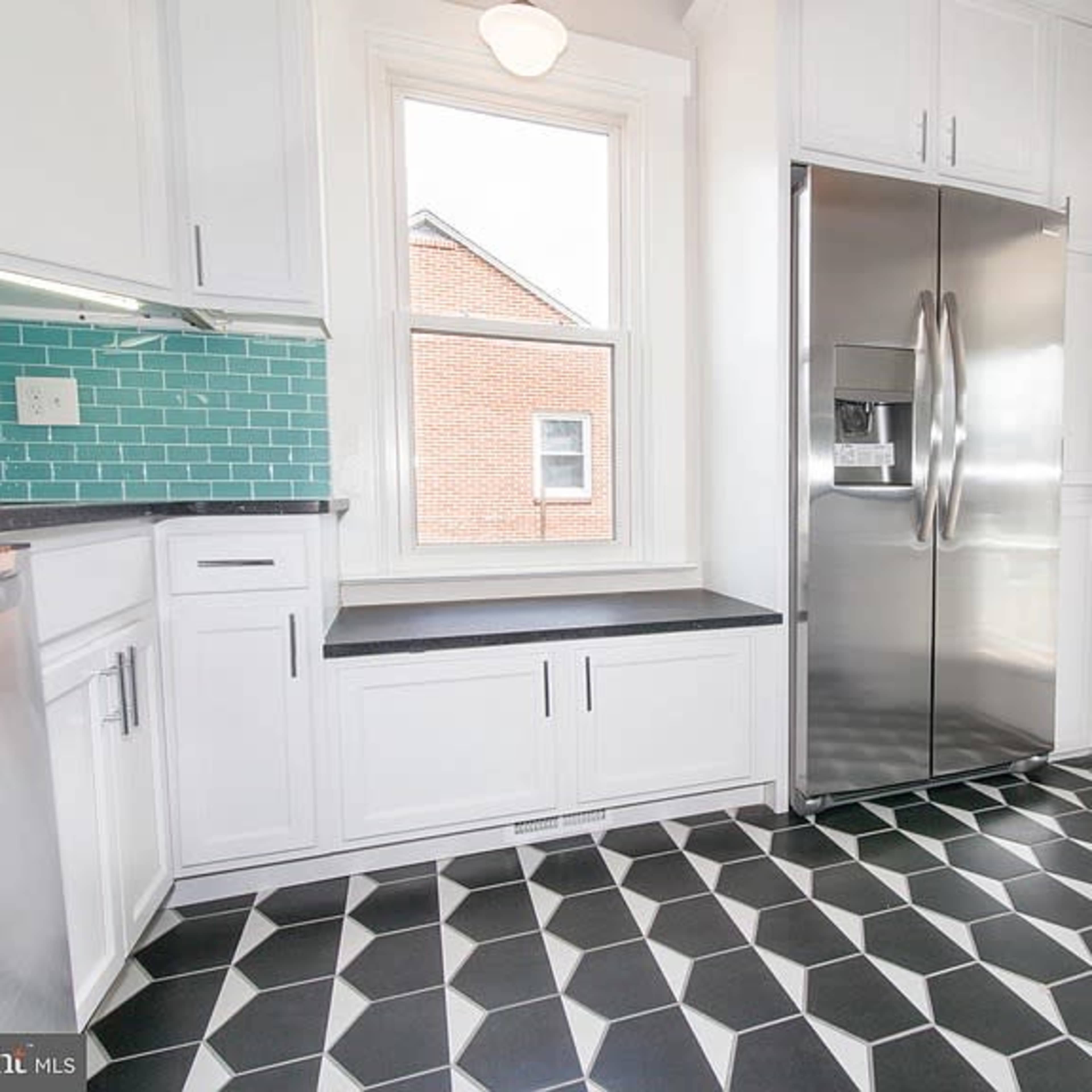 A modern kitchen features white cabinetry, a stainless steel refrigerator, and geometric black and white tile flooring.