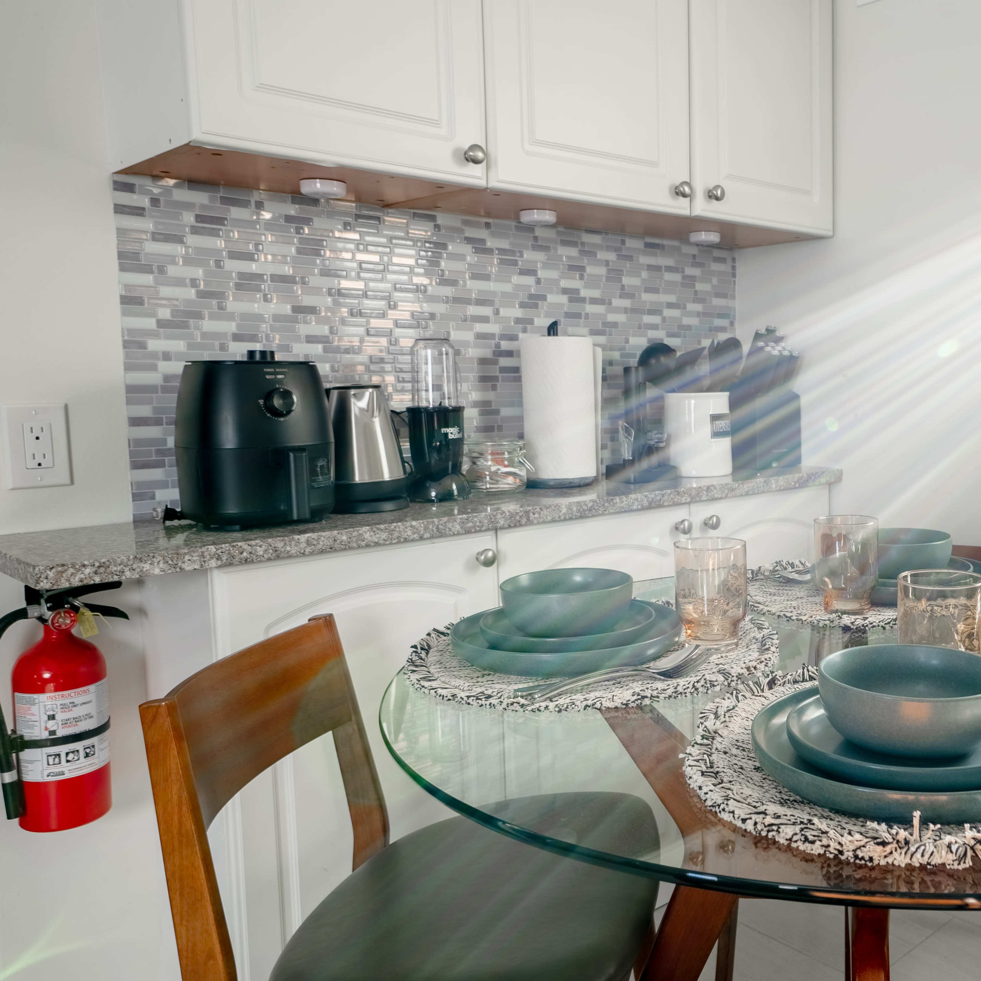 A well-set dining table with dark bowls and glasses is illuminated by sunlight in a modern kitchen.