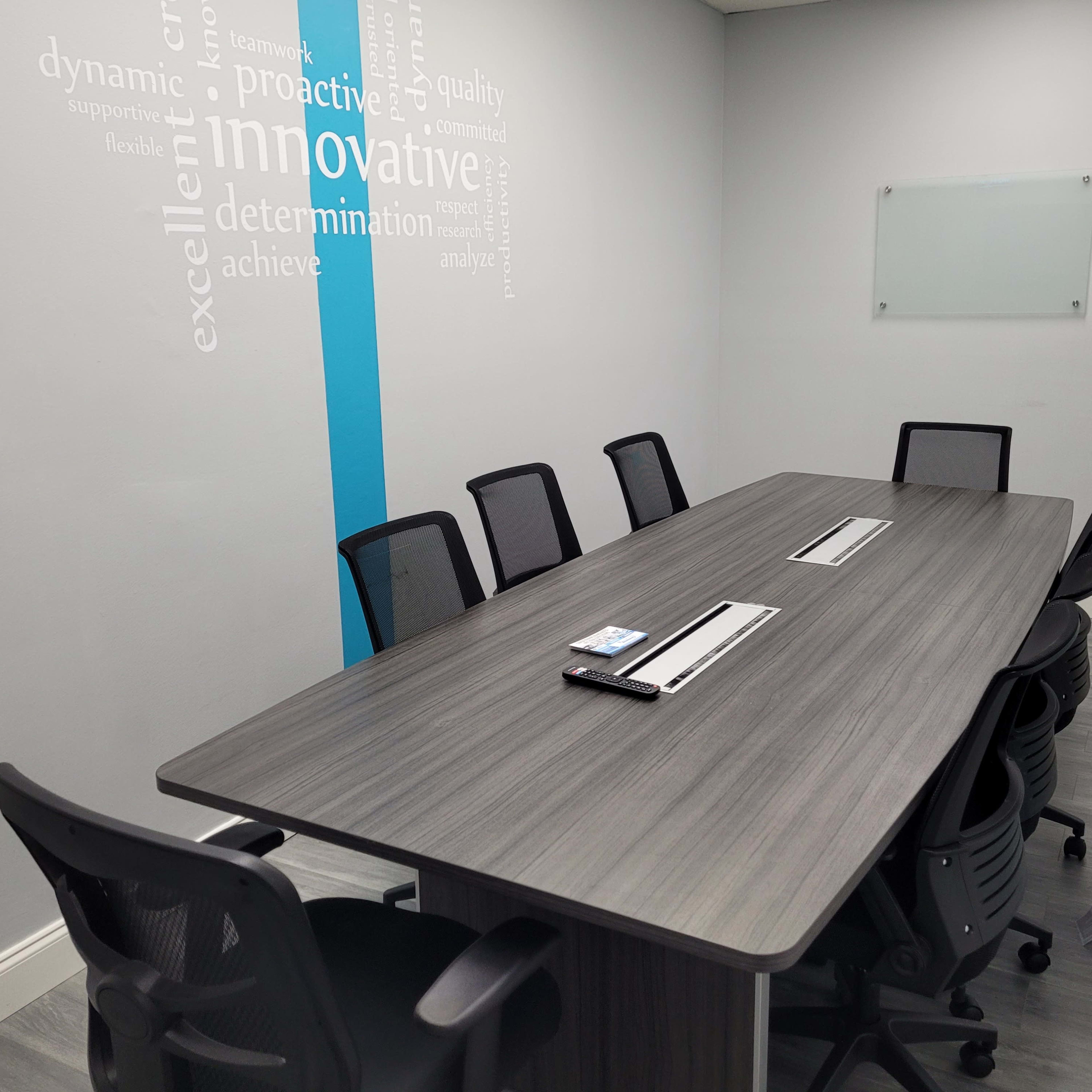 A modern conference room features a long table with multiple black chairs and wall text emphasizing business values.
