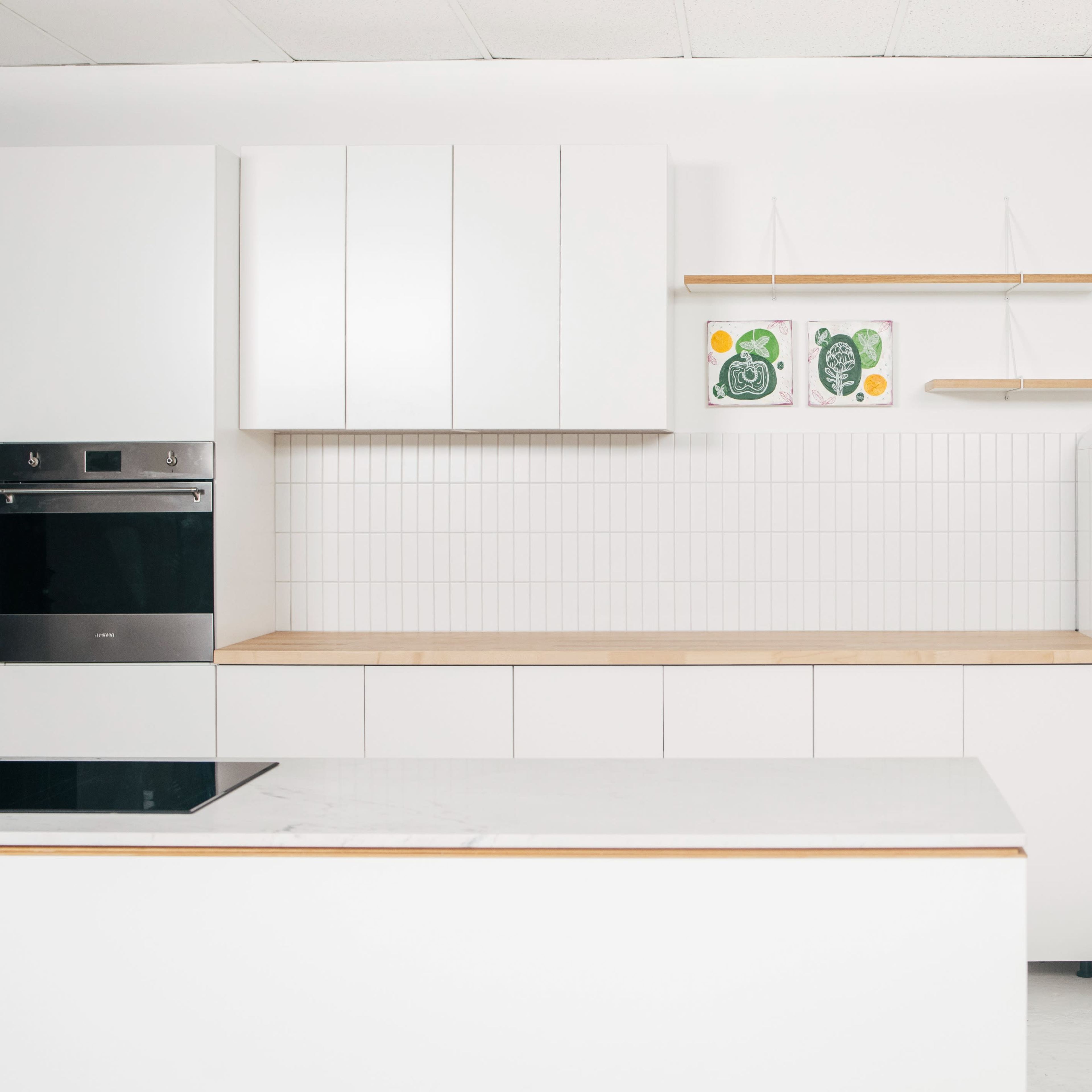 A modern kitchen featuring white cabinetry, a built-in oven, a minimalist open shelf, and a vintage-style white refrigerator.