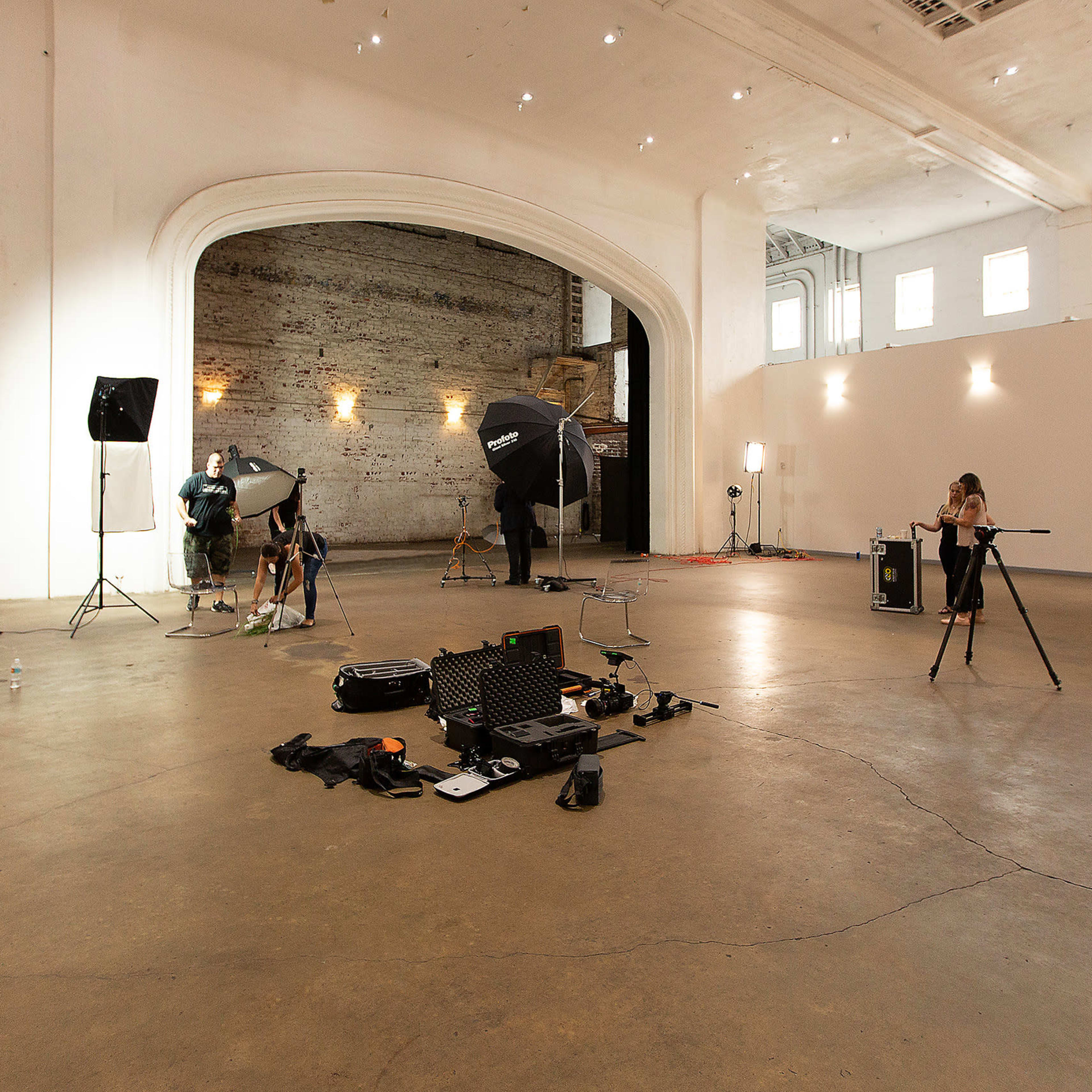A large, empty studio space is set up for a photoshoot, featuring lighting equipment and a photographer preparing their gear.