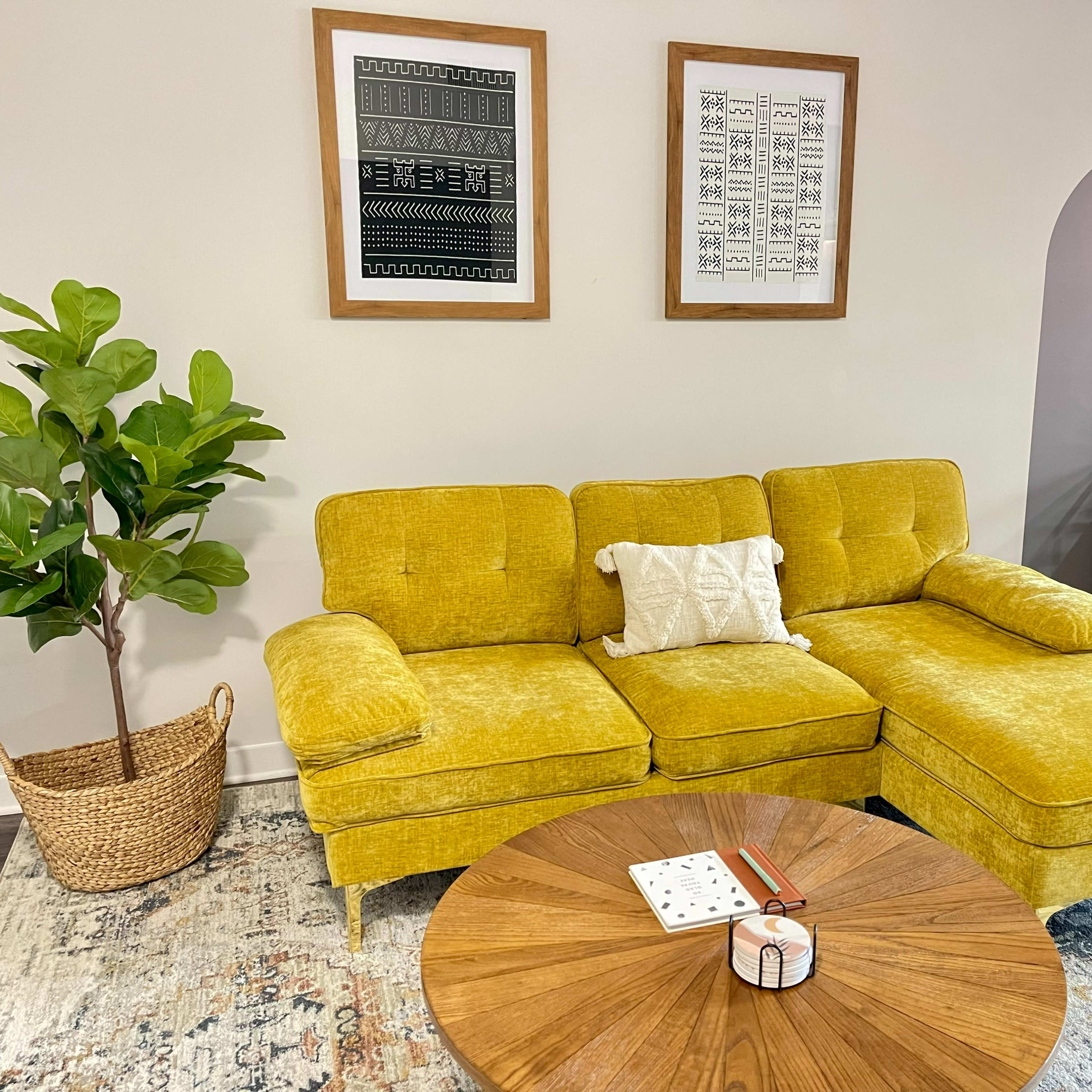 A yellow sectional sofa with a decorative pillow sits in a modern room, accompanied by a round wooden coffee table and a potted plant.