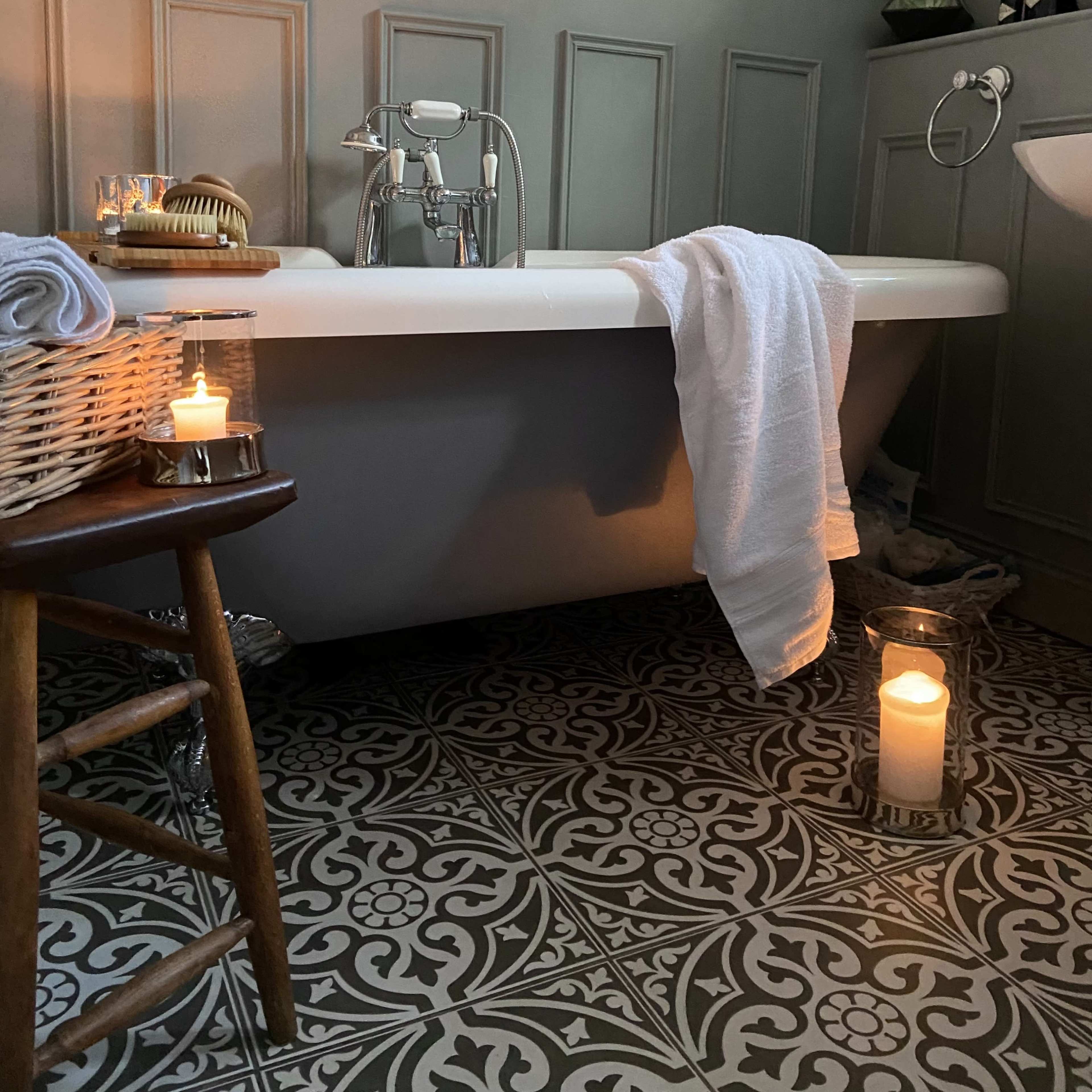 A modern bathroom with a freestanding bathtub, a wooden stool, candles, and decorative wall panels.