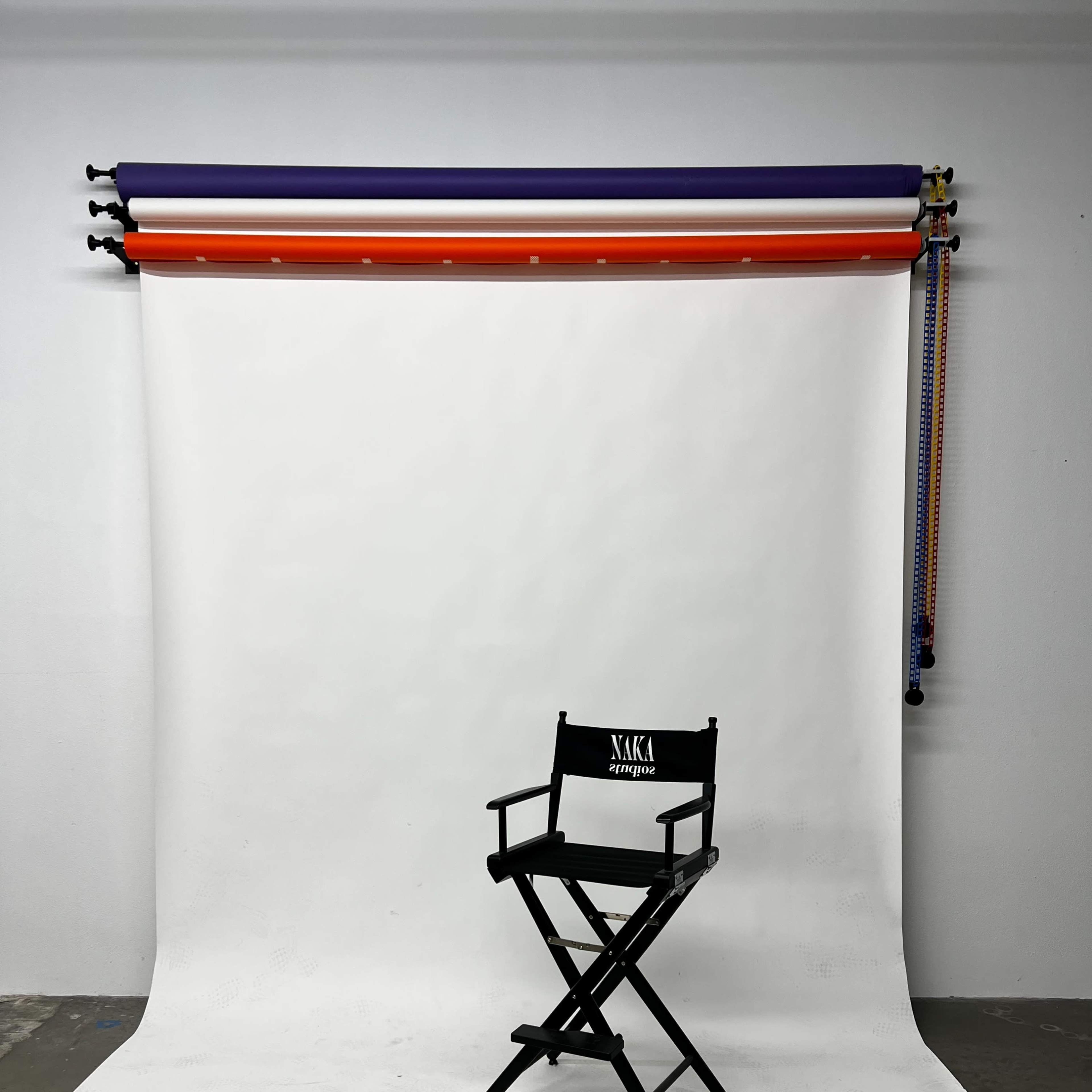 A black director's chair is positioned in front of a white backdrop with colored rolls at the top.