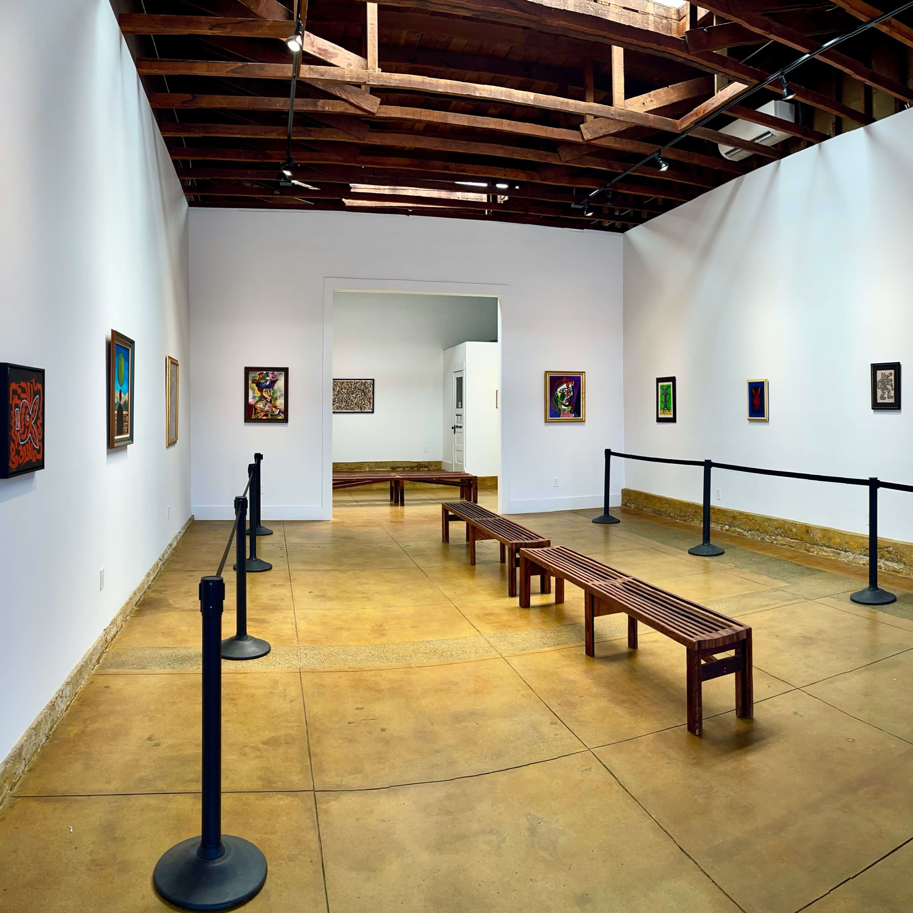 An art gallery with wooden benches and framed artworks displayed on the white walls.