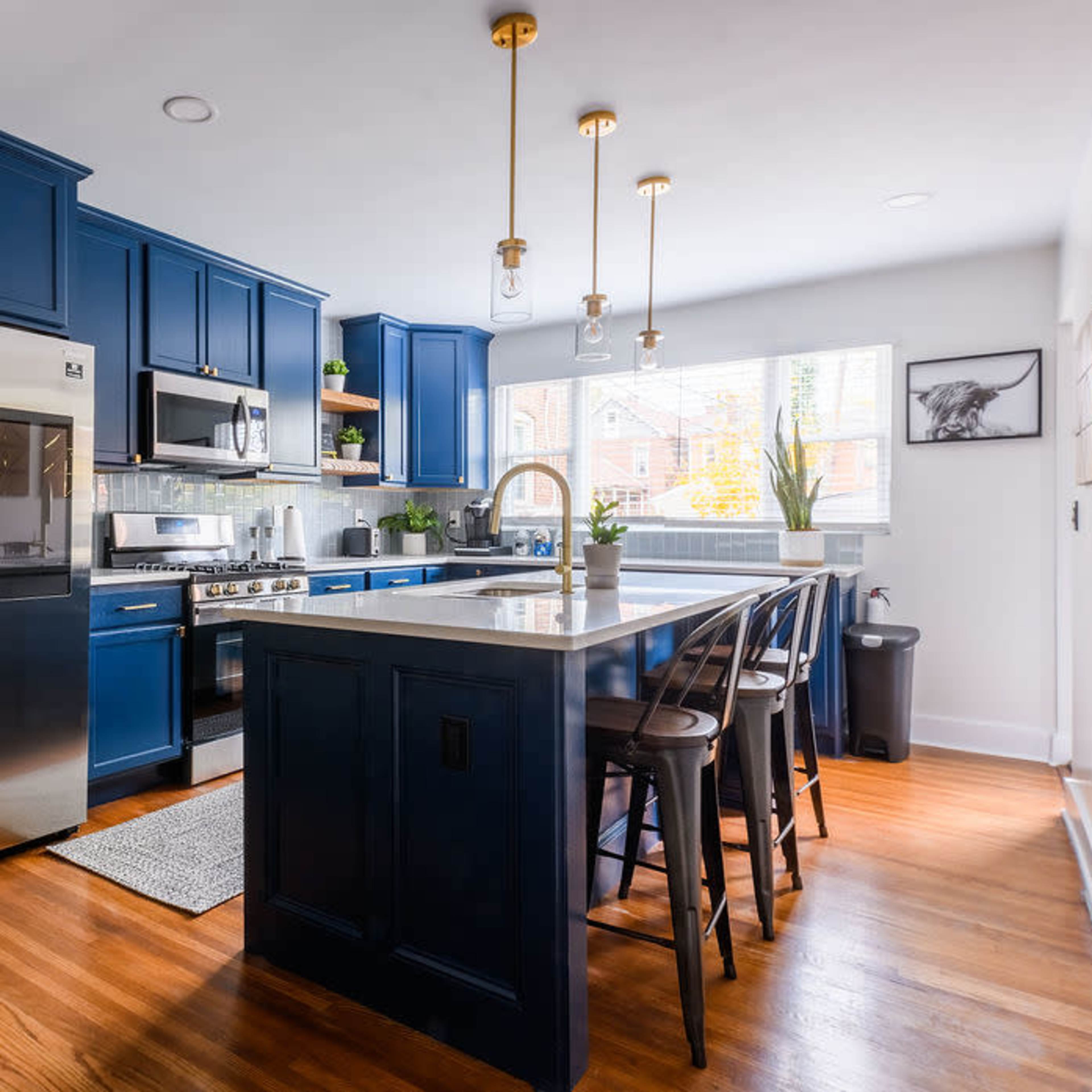 A modern kitchen featuring blue cabinetry, stainless steel appliances, a central island with seating, and natural light streaming in from a window.