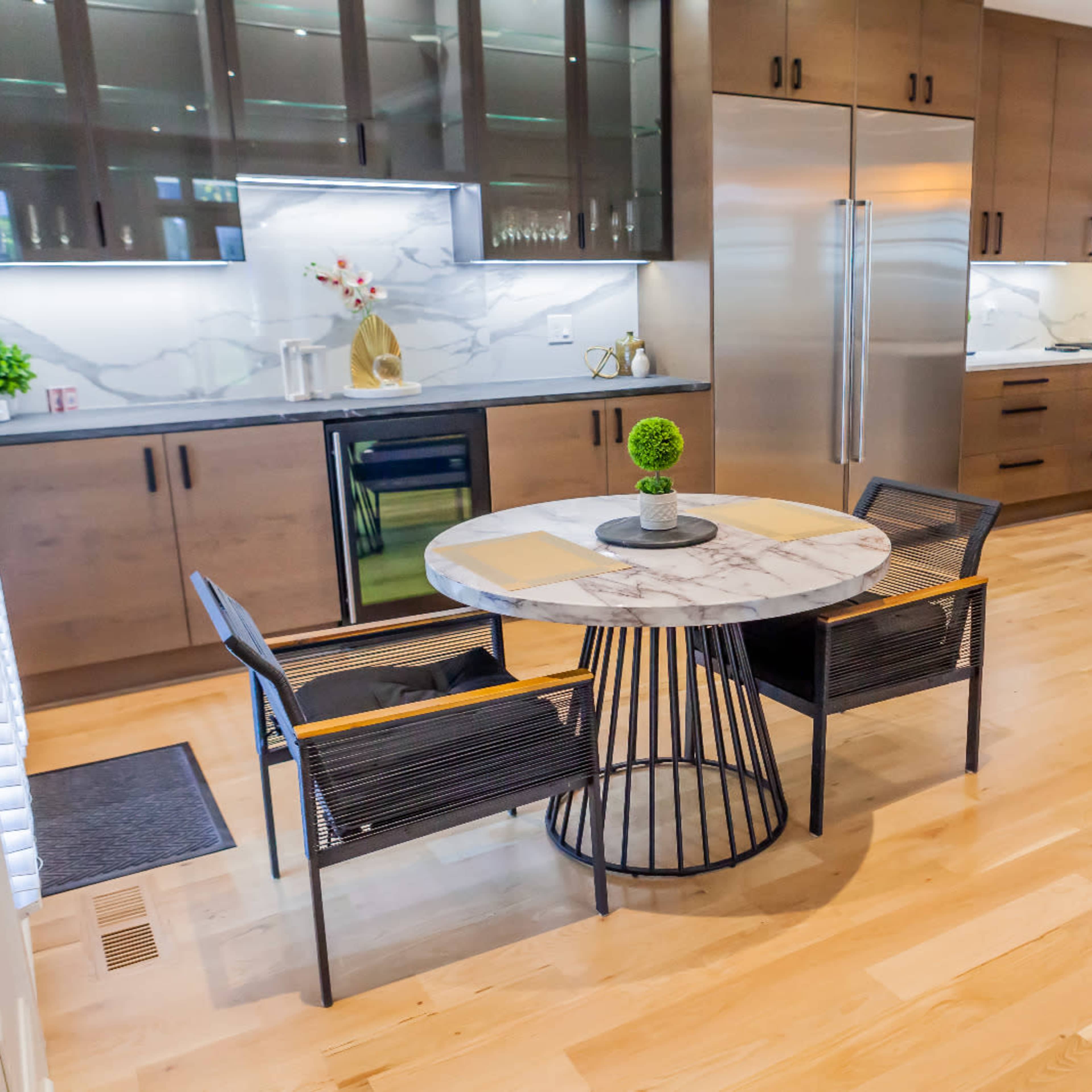 A modern kitchen with a marble dining table surrounded by black chairs, featuring wooden cabinets and stainless steel appliances.