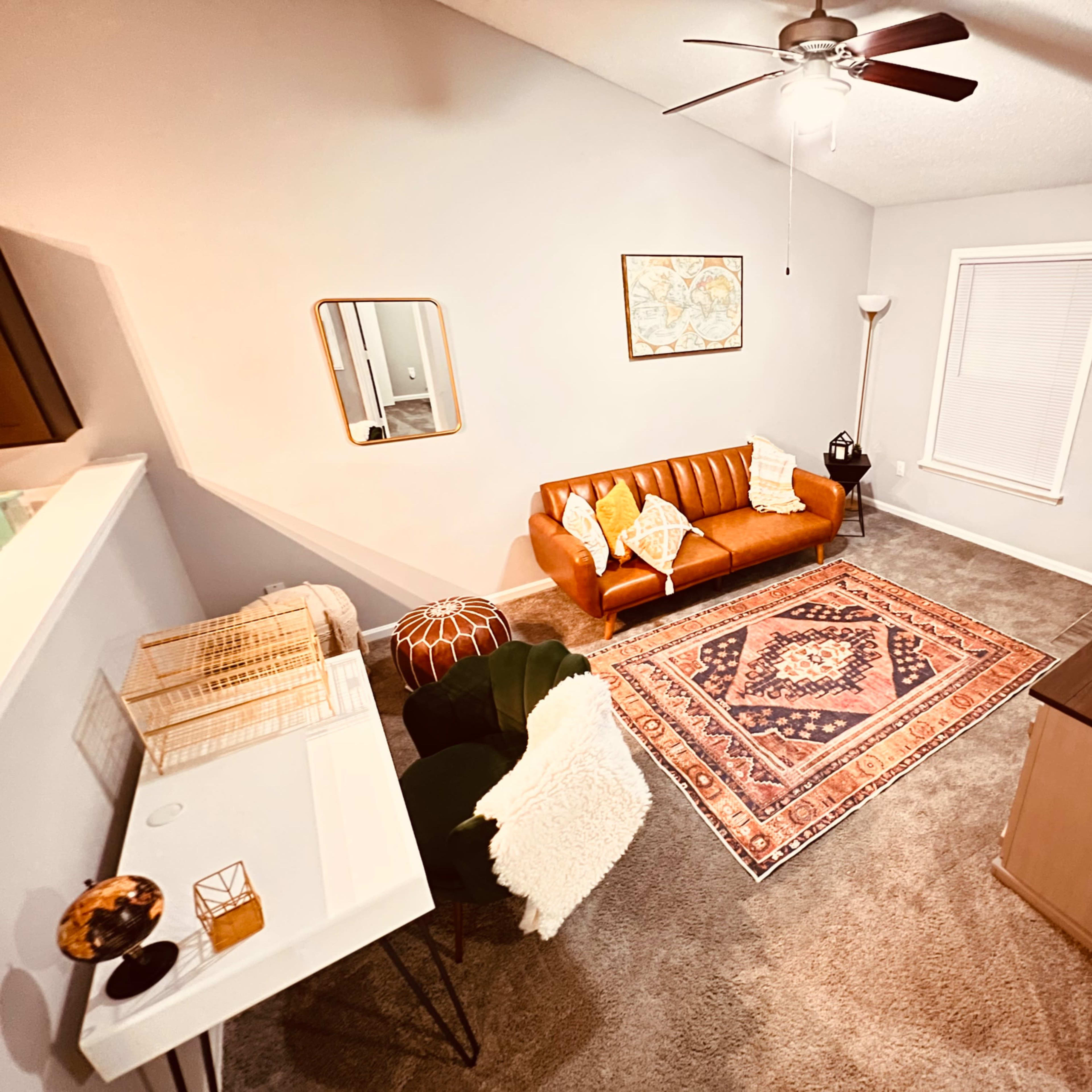 A cozy living room with a brown leather sofa, a patterned area rug, and a television, complemented by a floor lamp and decorative elements.