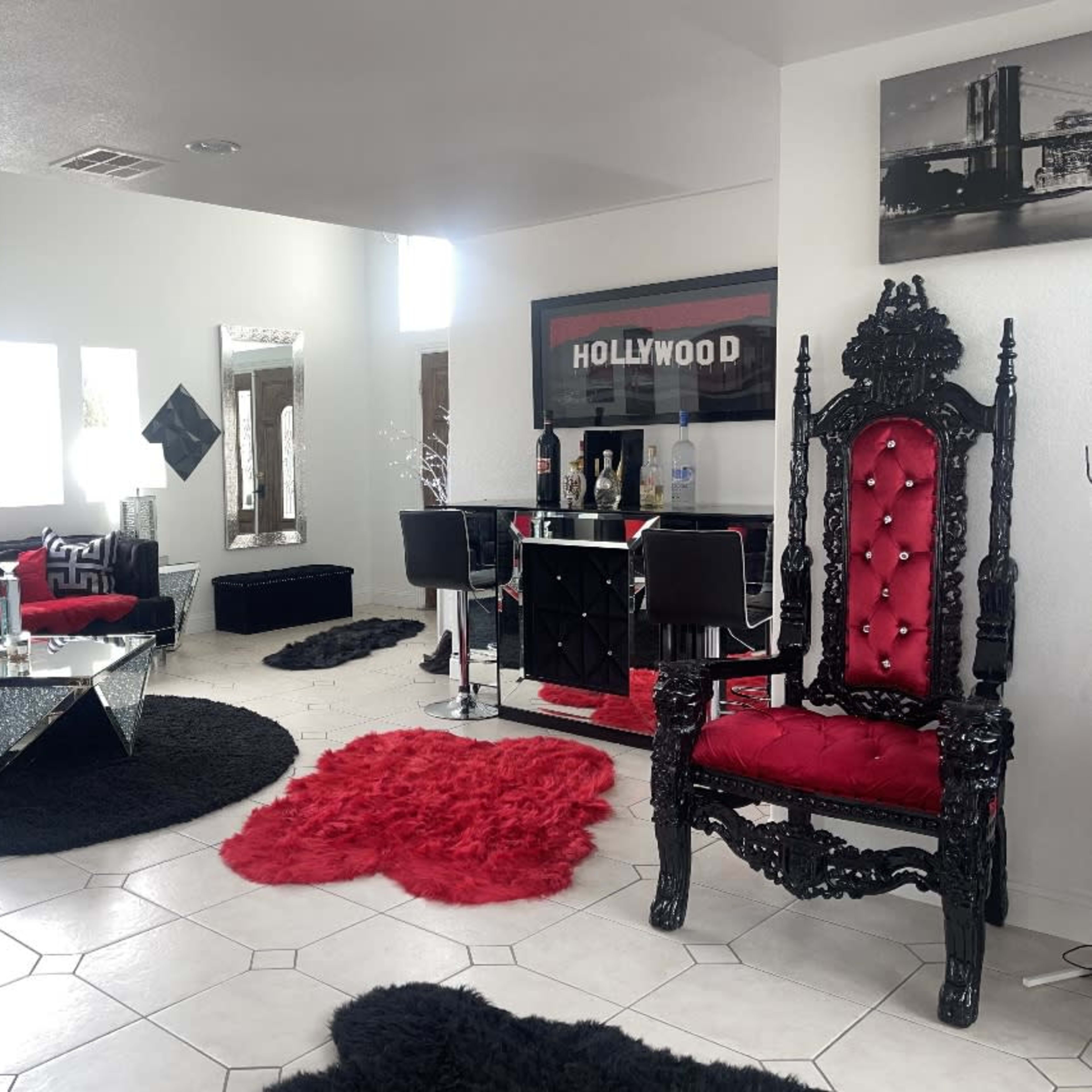 The room features modern furnishings with a black and red color scheme, including a large ornate chair, a glass coffee table, and a bar area.