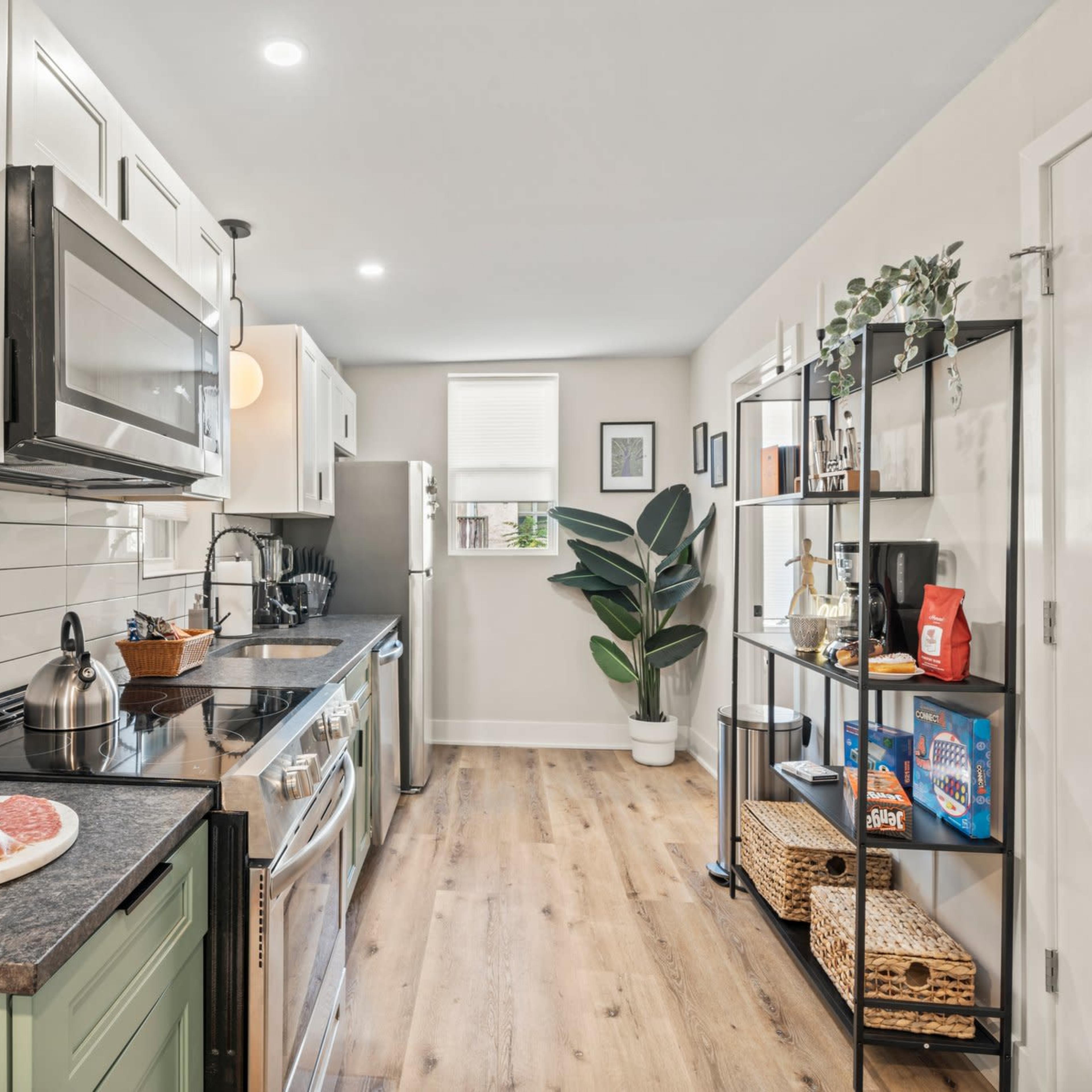 A modern kitchen features stainless steel appliances, a wooden floor, and a variety of shelving displaying food items and plants.
