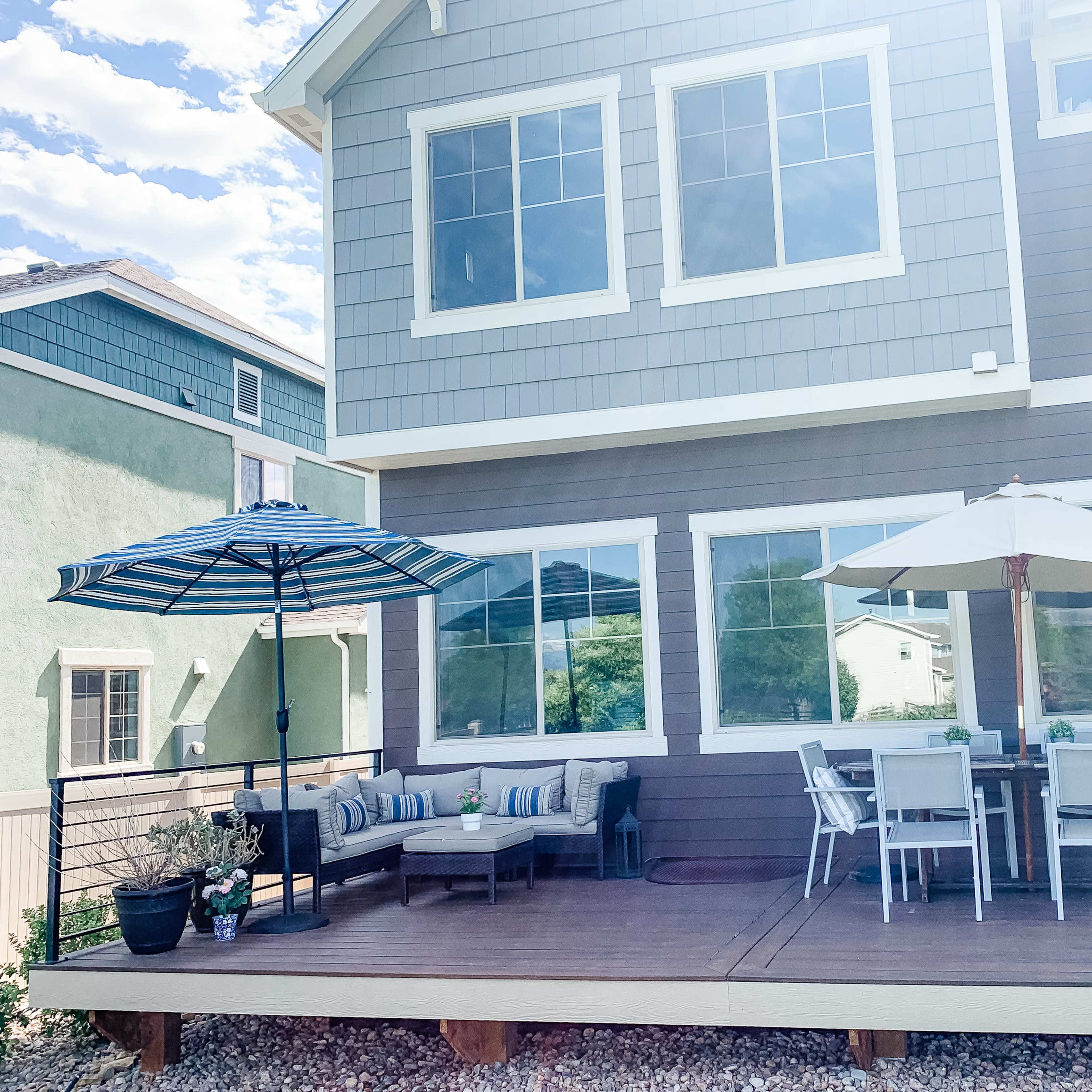 A house with a large deck featuring a dining table set under an umbrella and a seating area with a couch and an umbrella.