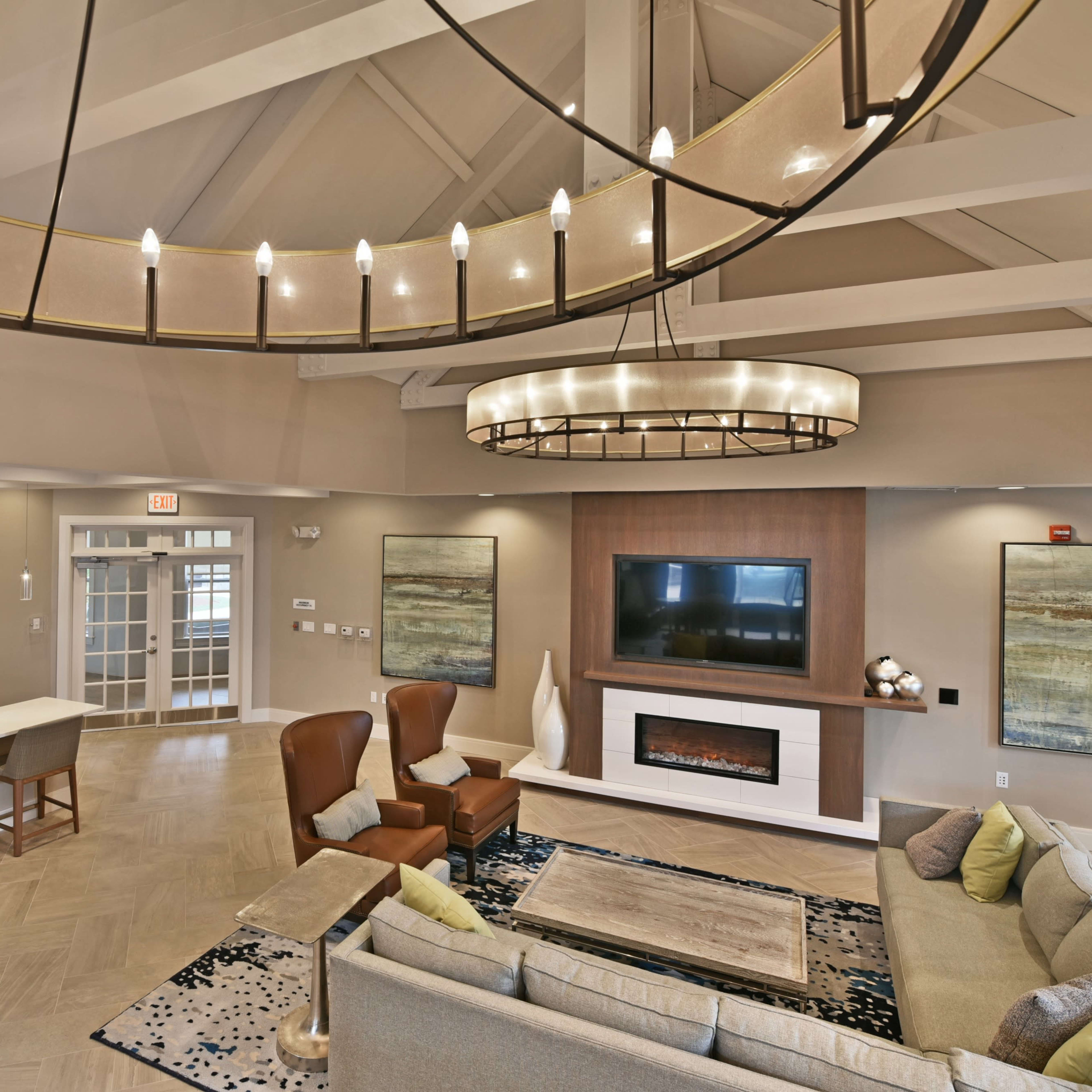 A modern living room with a high ceiling, featuring a comfortable seating area, a wall-mounted television, and a decorative fireplace.