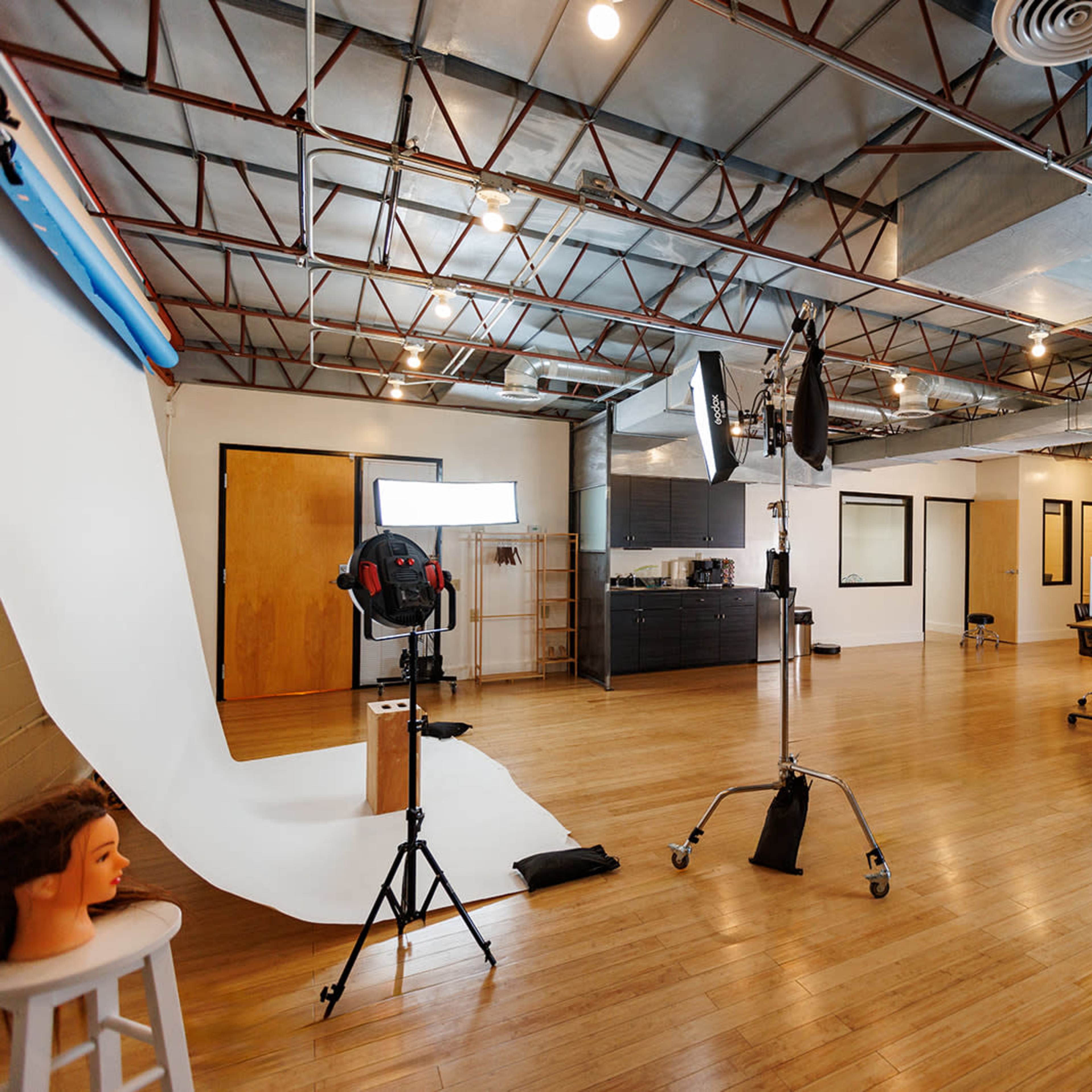 A spacious photography studio with a white backdrop, lighting equipment, and wooden flooring.