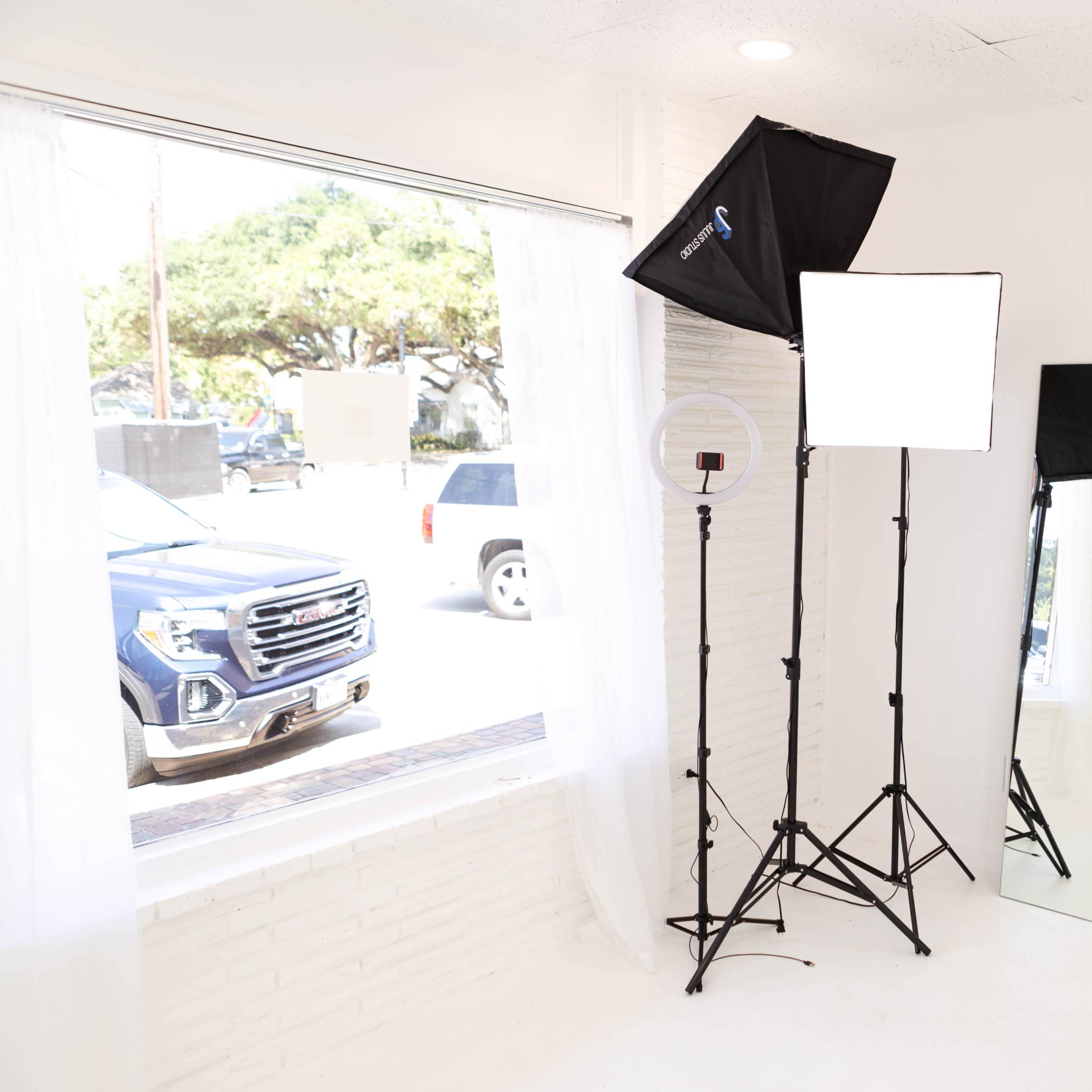 A bright studio space featuring two lighting setups and a large mirror next to a window.