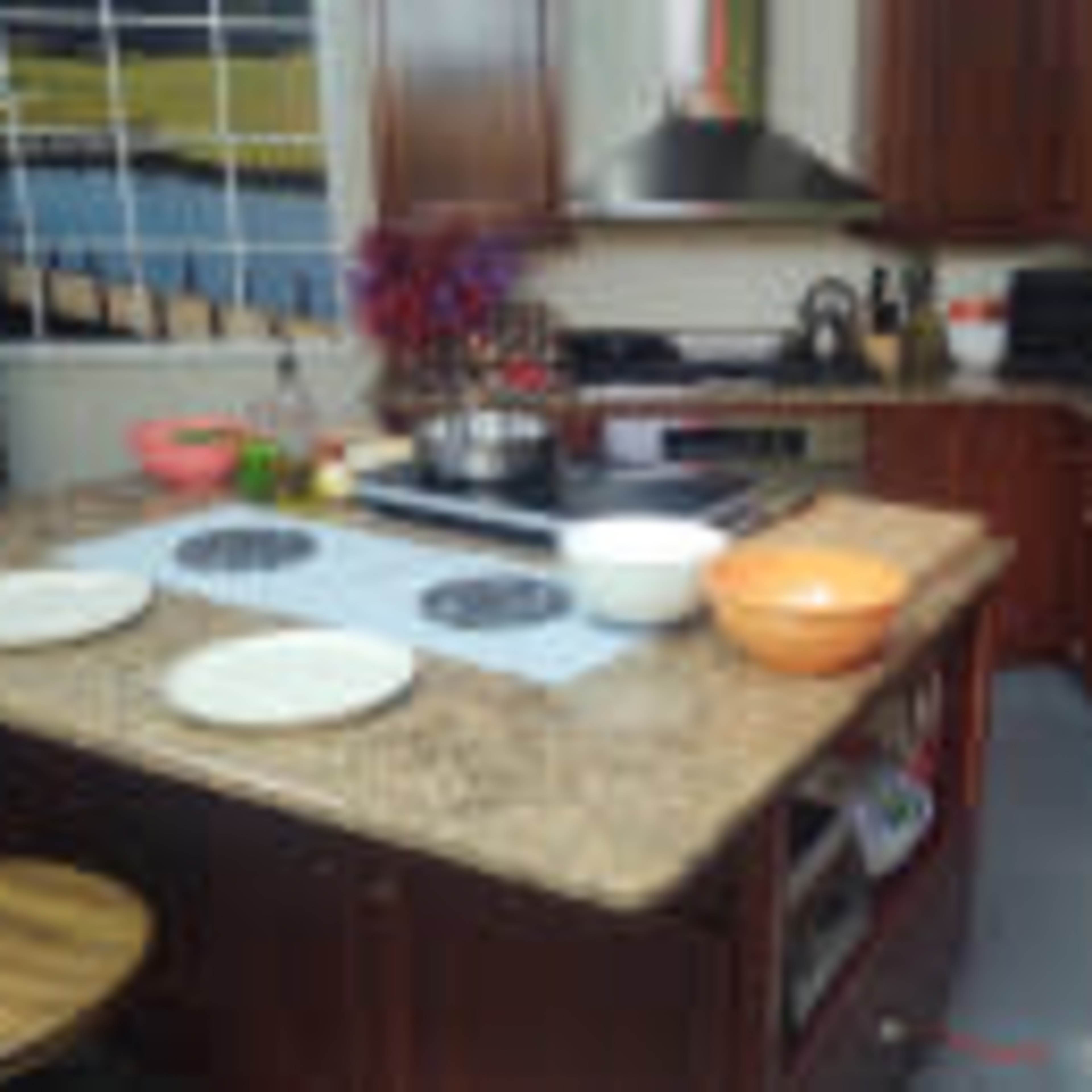 A kitchen features wooden cabinets, a granite countertop with cooking utensils and plates, and an electric stove.