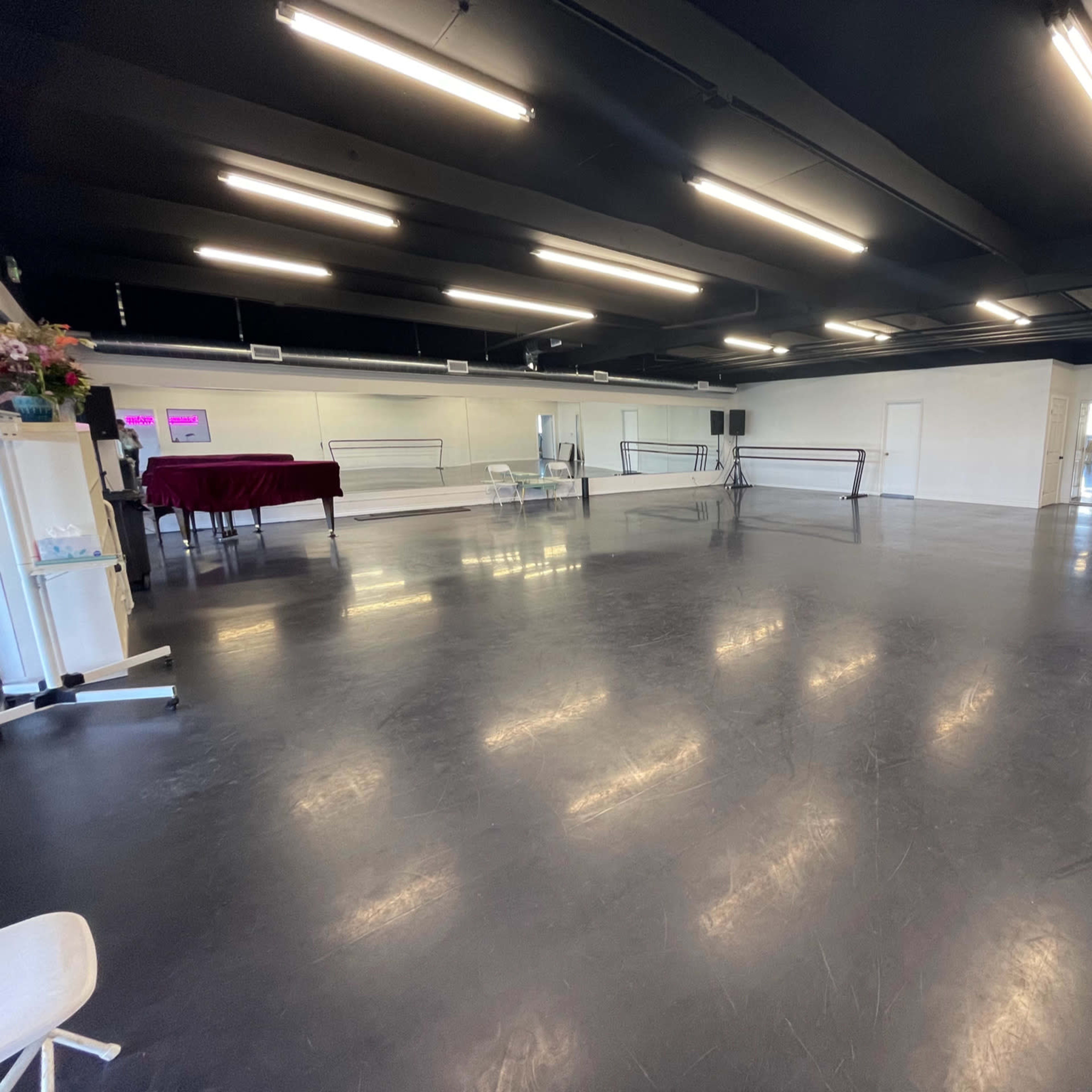 A spacious dance studio with a mirrored wall, ballet barres, and a polished floor under bright overhead lighting.