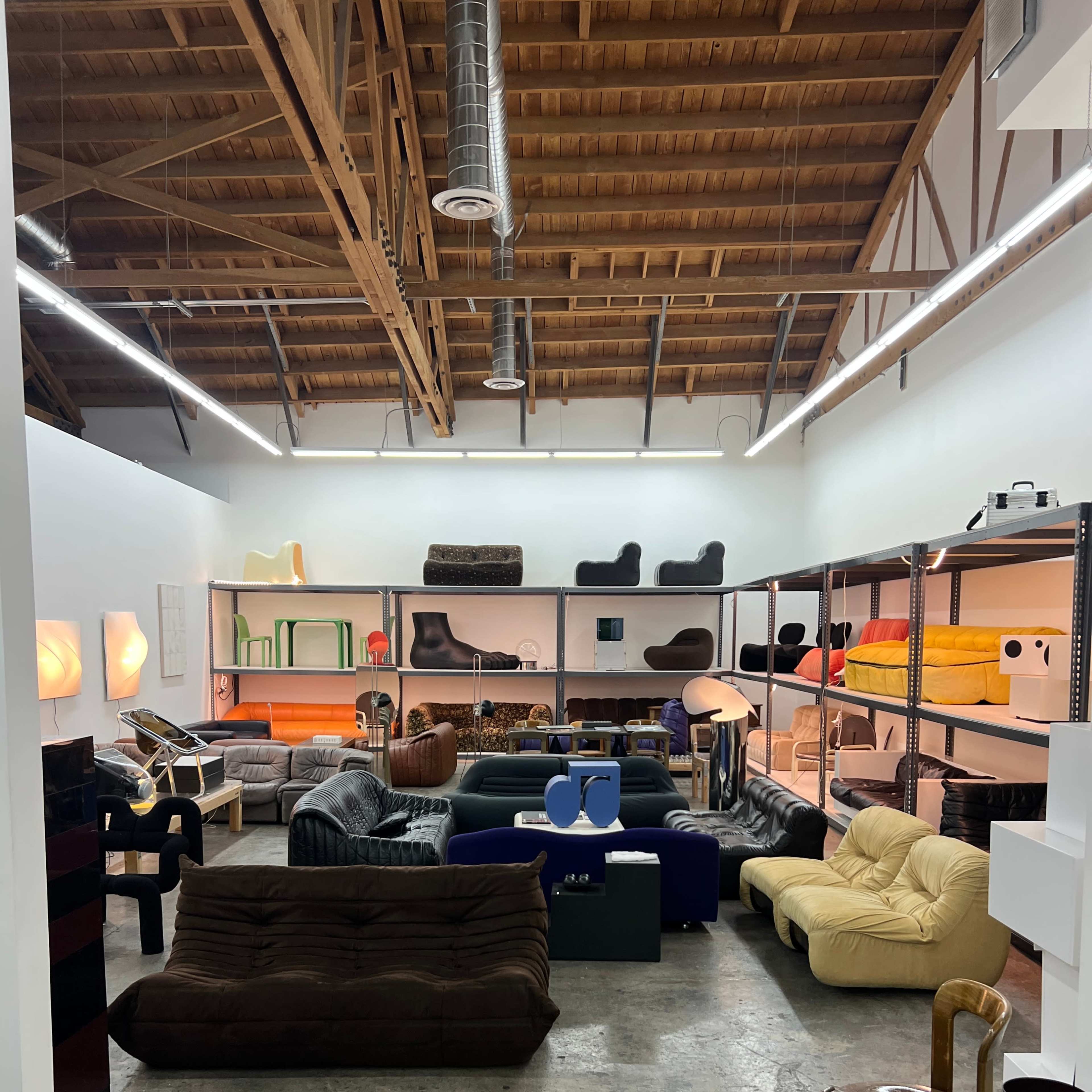 A spacious interior filled with various styles of furniture, including couches and chairs, arranged in a contemporary setting with exposed wooden beams.