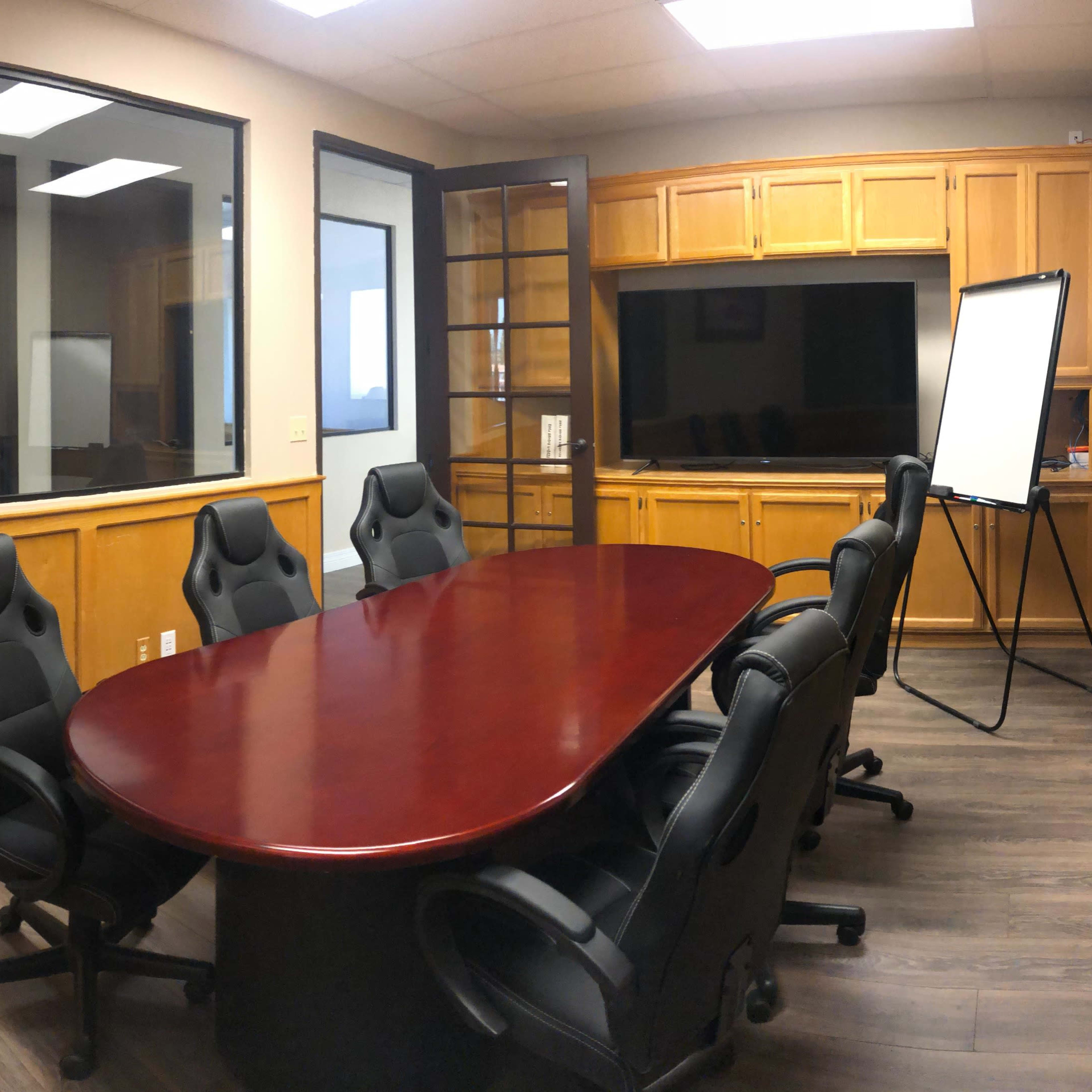 A conference room with a large round table, several black office chairs, a whiteboard on a stand, and wooden cabinetry along the walls.