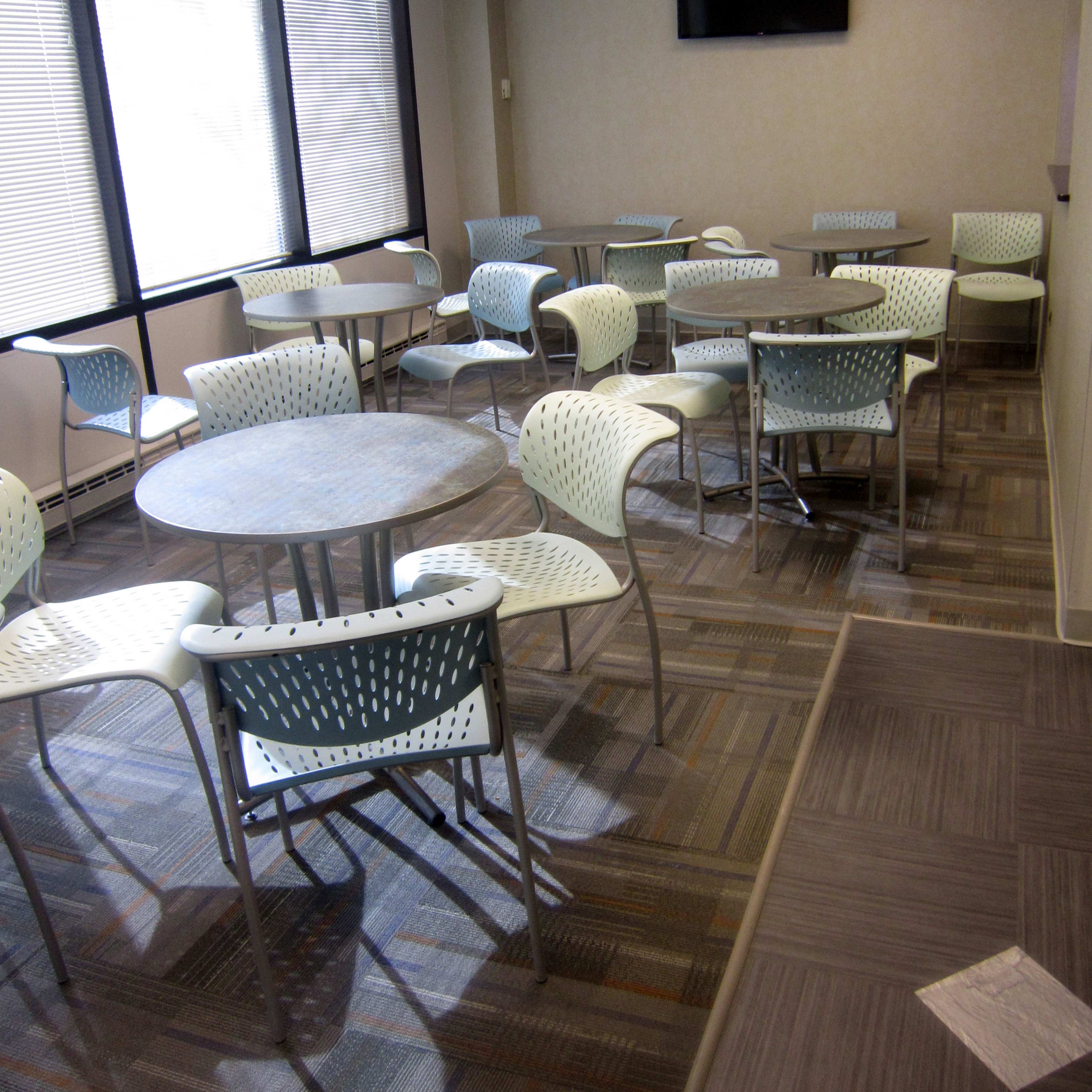 A semi-empty room with multiple round tables surrounded by metal and plastic chairs, and a small television mounted on the wall.