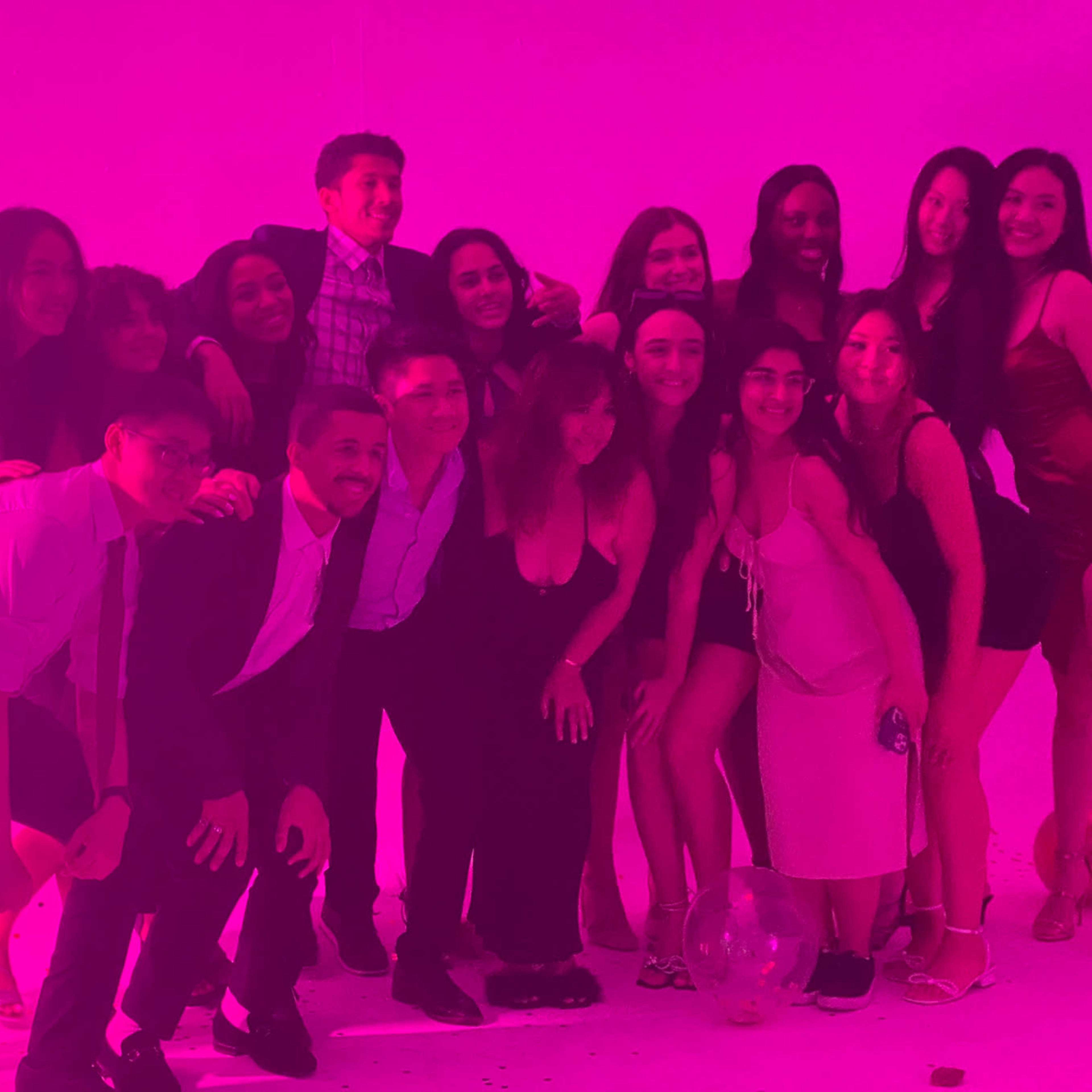 A group of young people poses together in front of a pink backdrop at a social event.