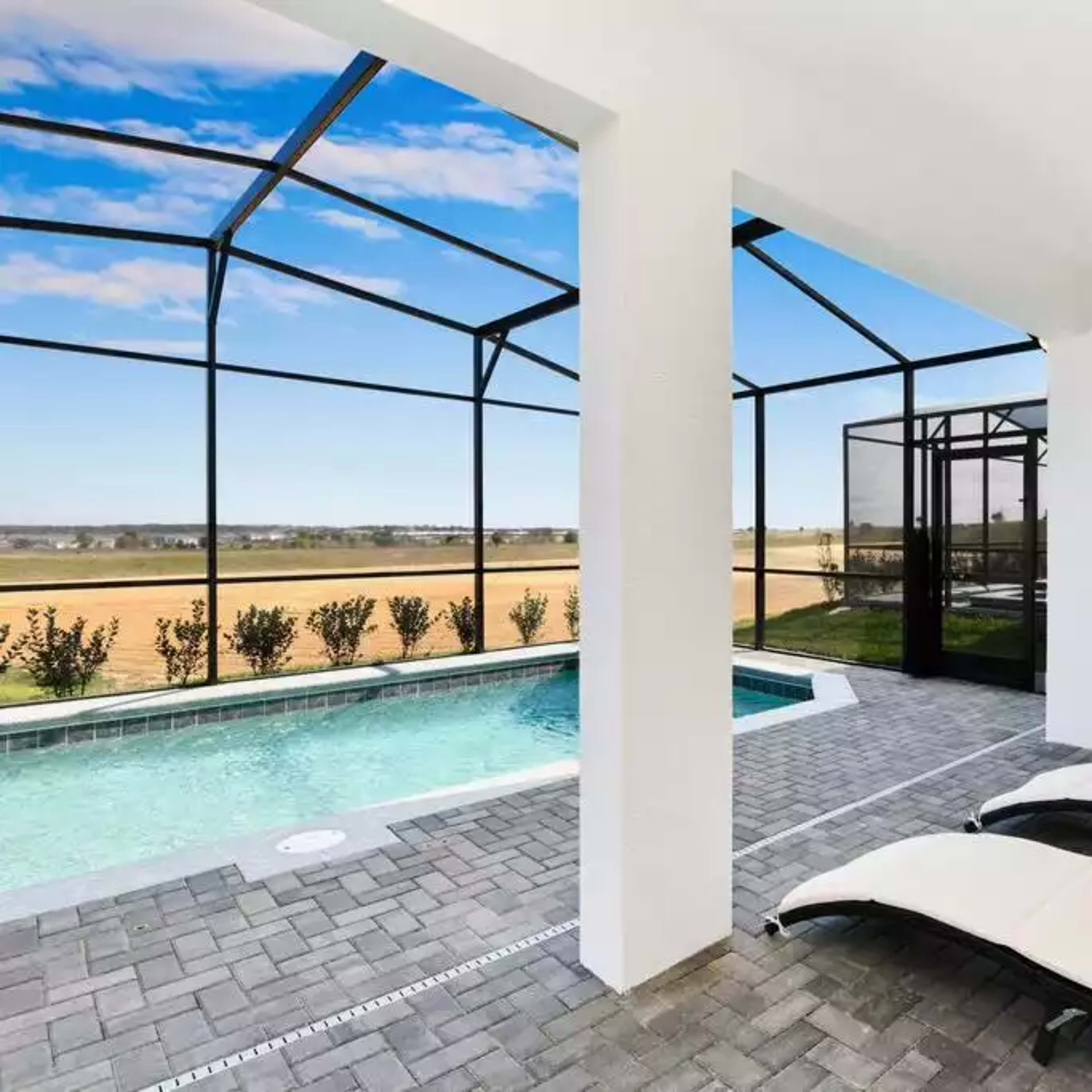 A modern outdoor space with two lounge chairs beside a swimming pool, enclosed by a mesh screen and overlooking a grassy landscape.