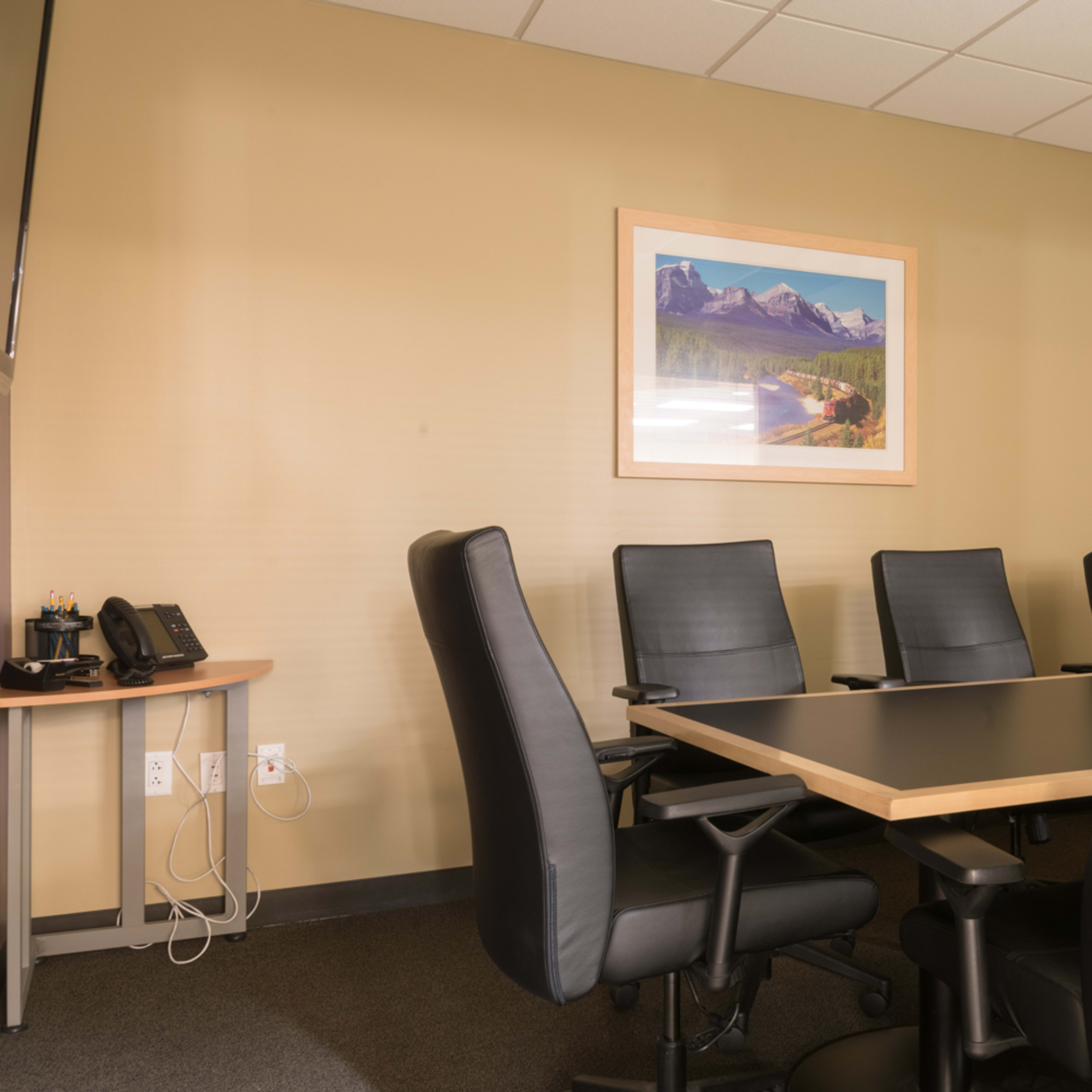 A conference room features a large table surrounded by several black leather chairs and a landscape painting on the wall.