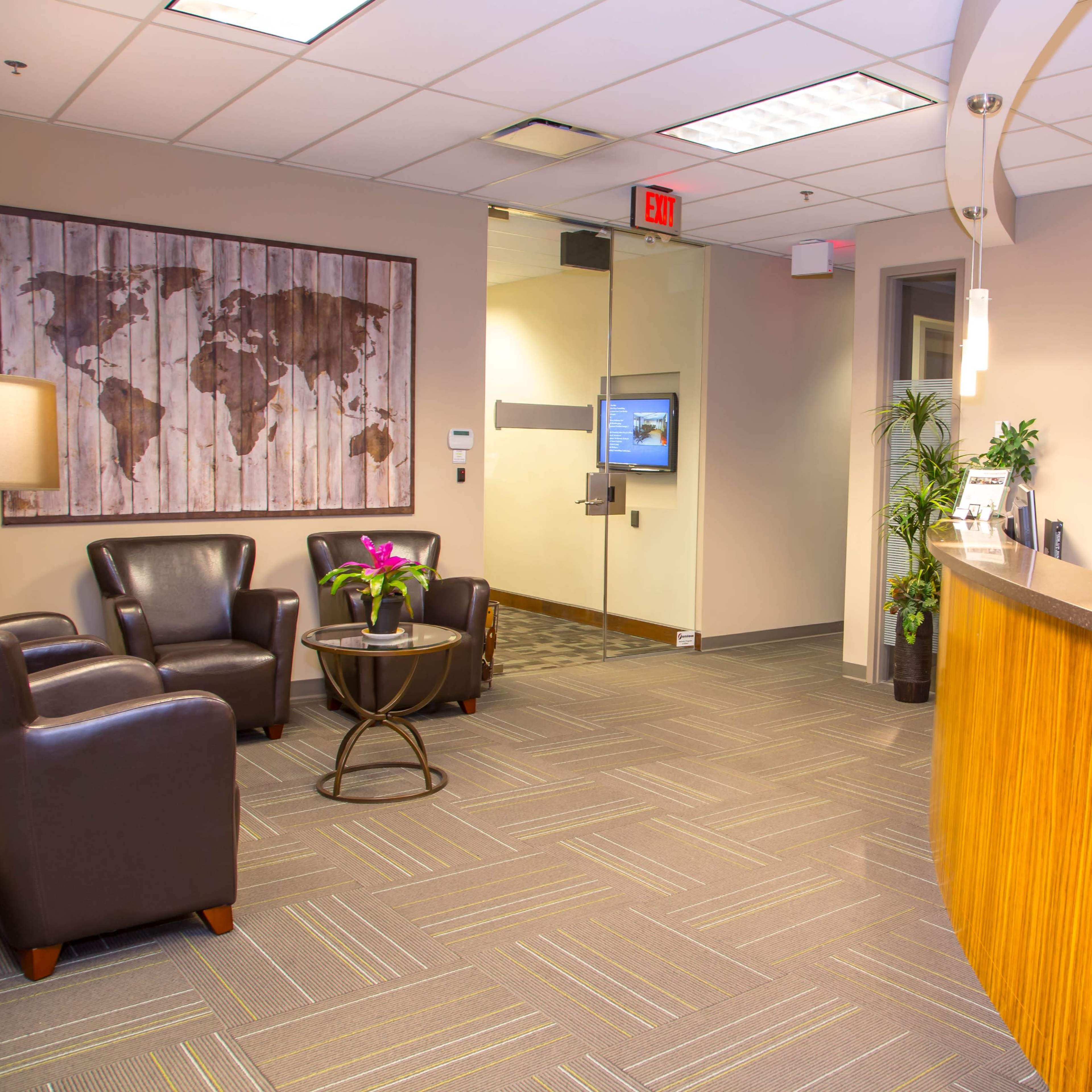 A modern reception area with a curved wooden desk, leather chairs, a coffee table, a mural of a world map on the wall, and plants in pots.