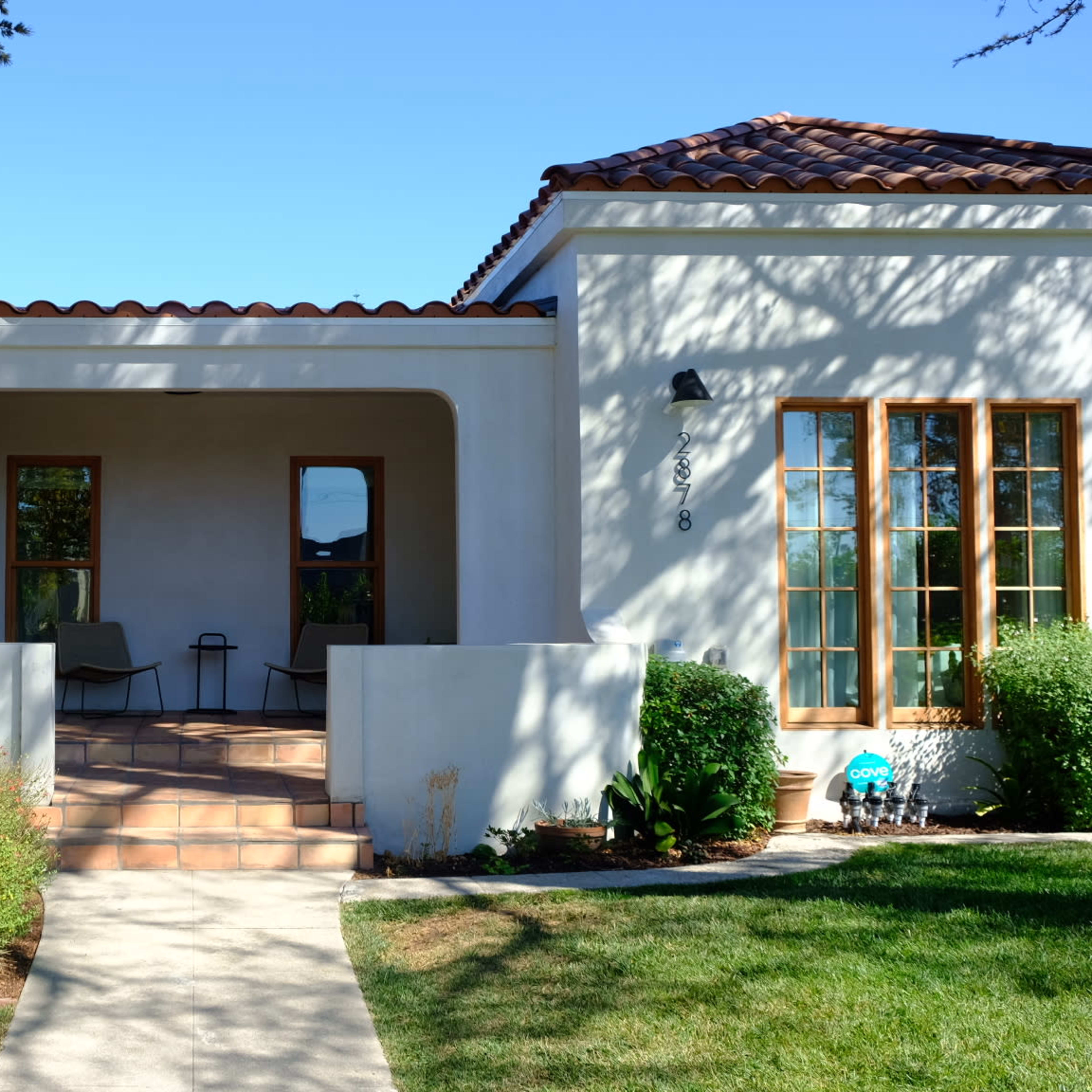 A Spanish-style house with a tiled roof and a walkway leading to a front porch shaded by trees.