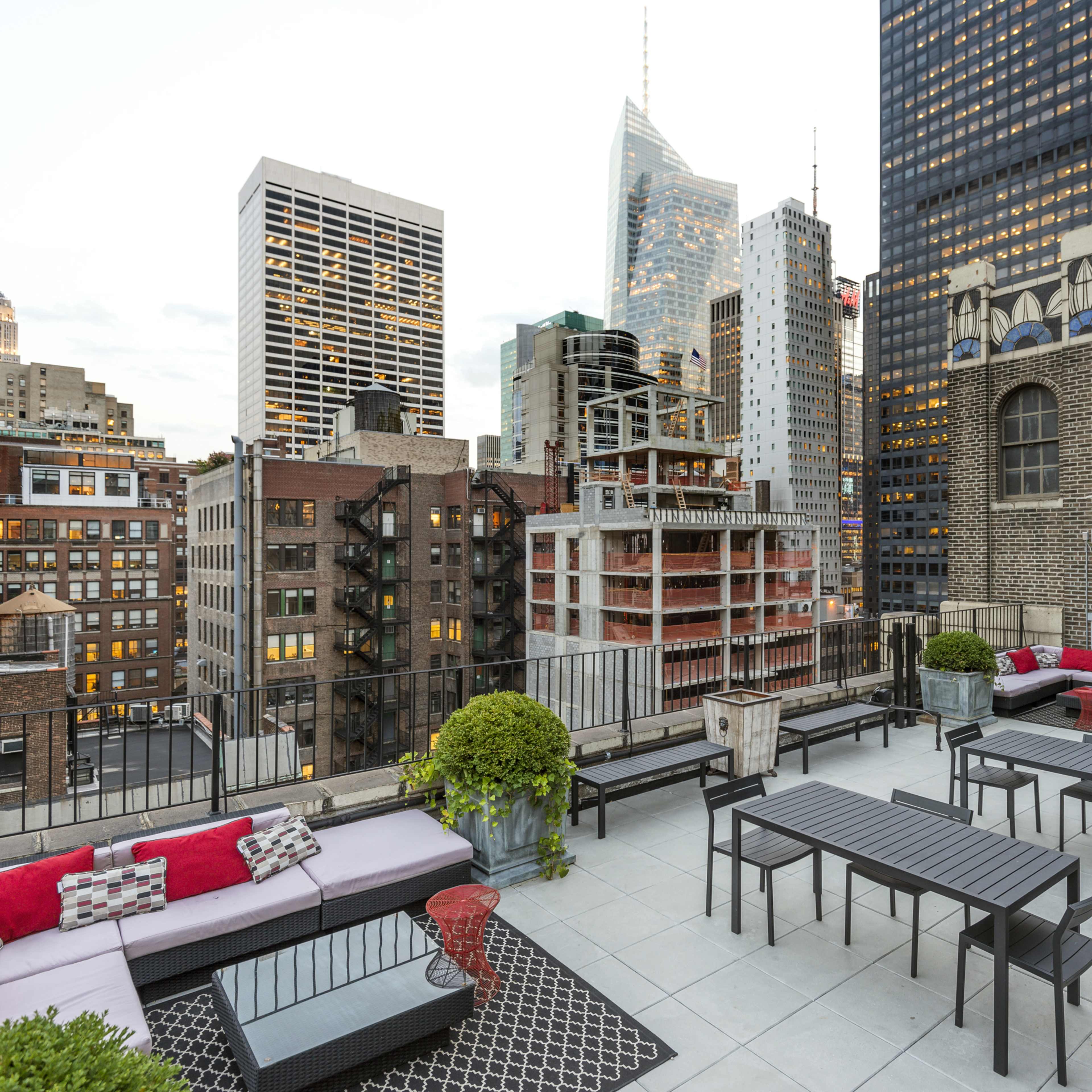 A rooftop terrace with modern furniture, overlooking a city skyline that includes the Empire State Building.