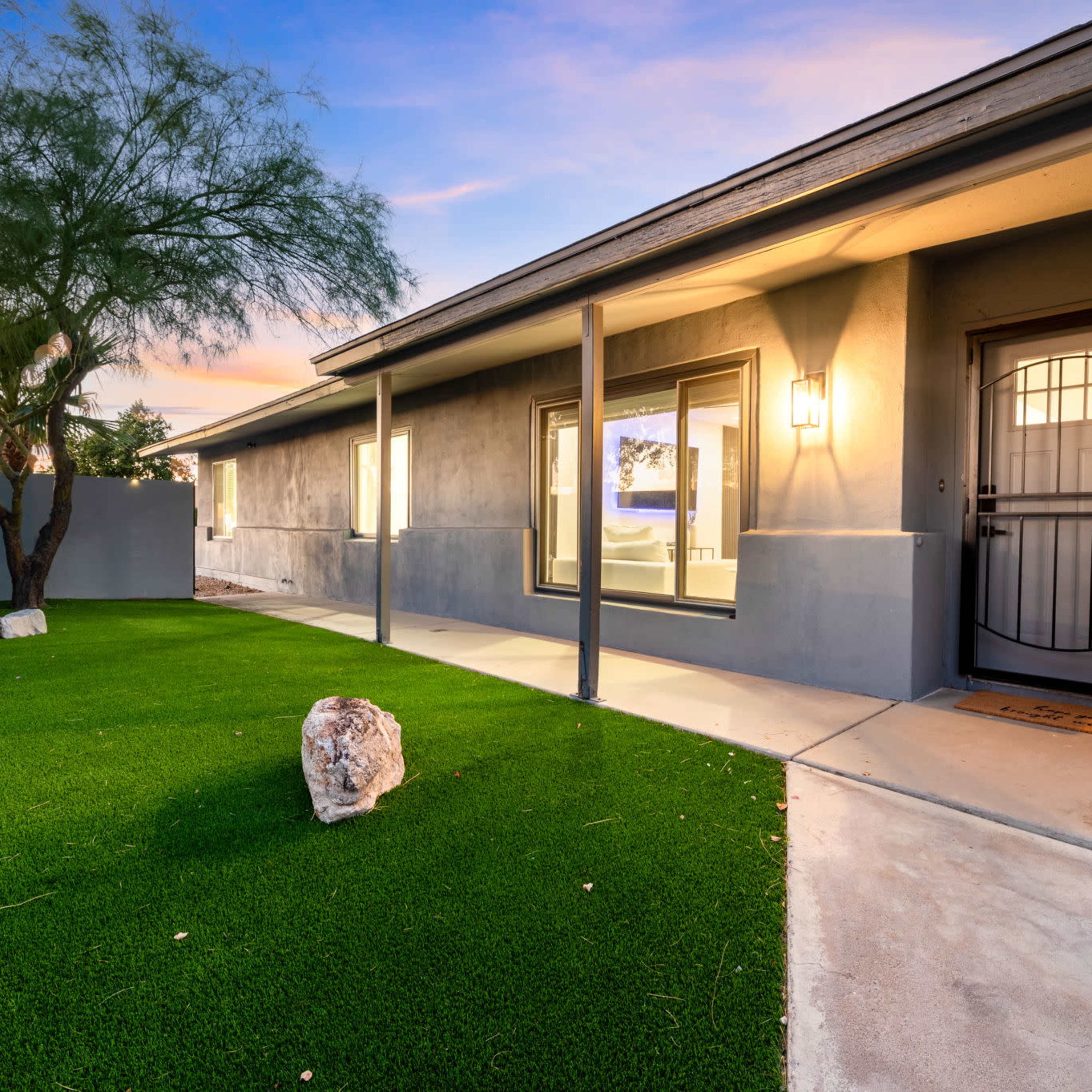 A modern house exterior with a landscaped path, artificial turf, and a small rock feature near the entrance.