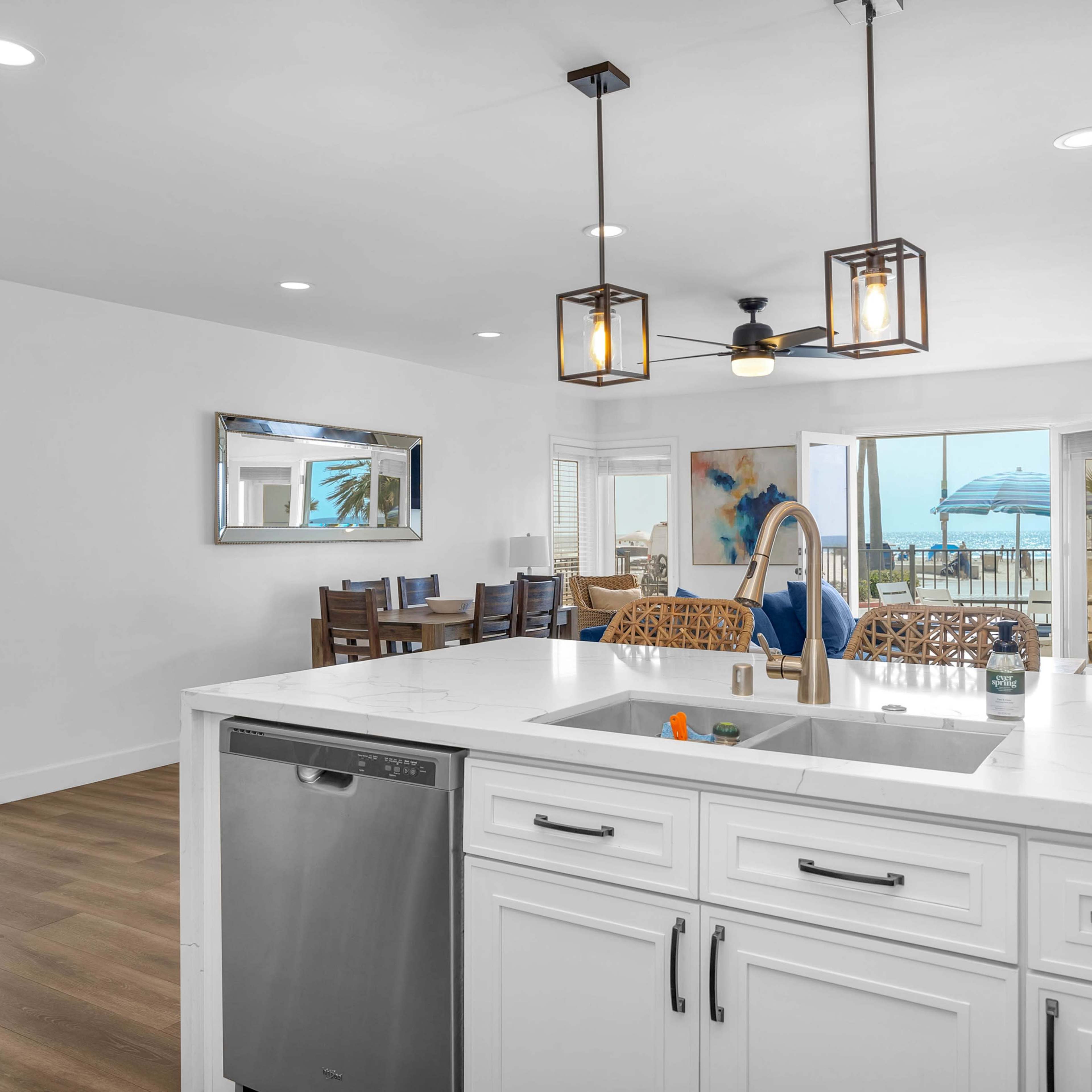 A modern kitchen with white cabinetry and a visible living area that opens up to a deck with views of the water.