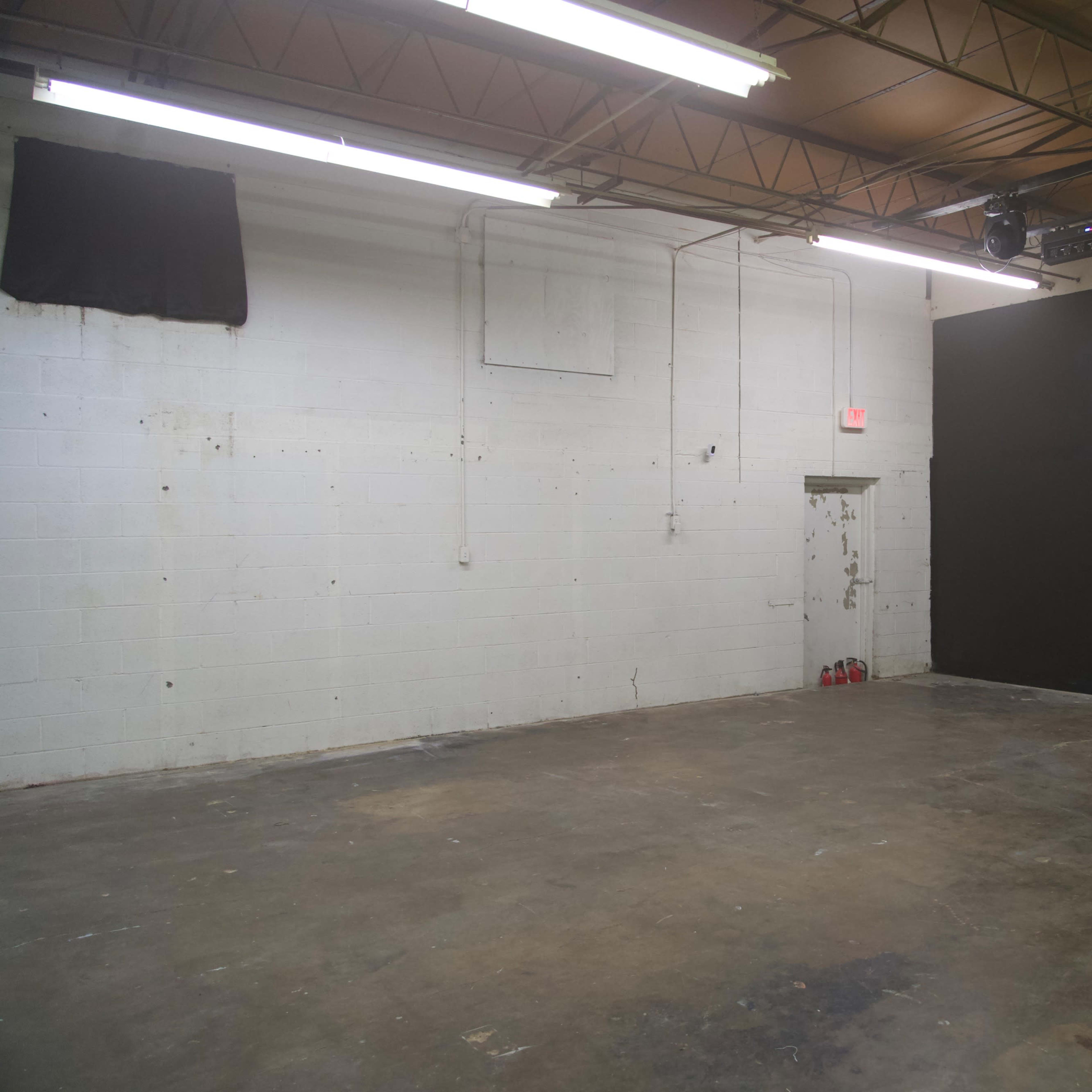 An empty room with a concrete floor, white walls, and a large black wall at one end.