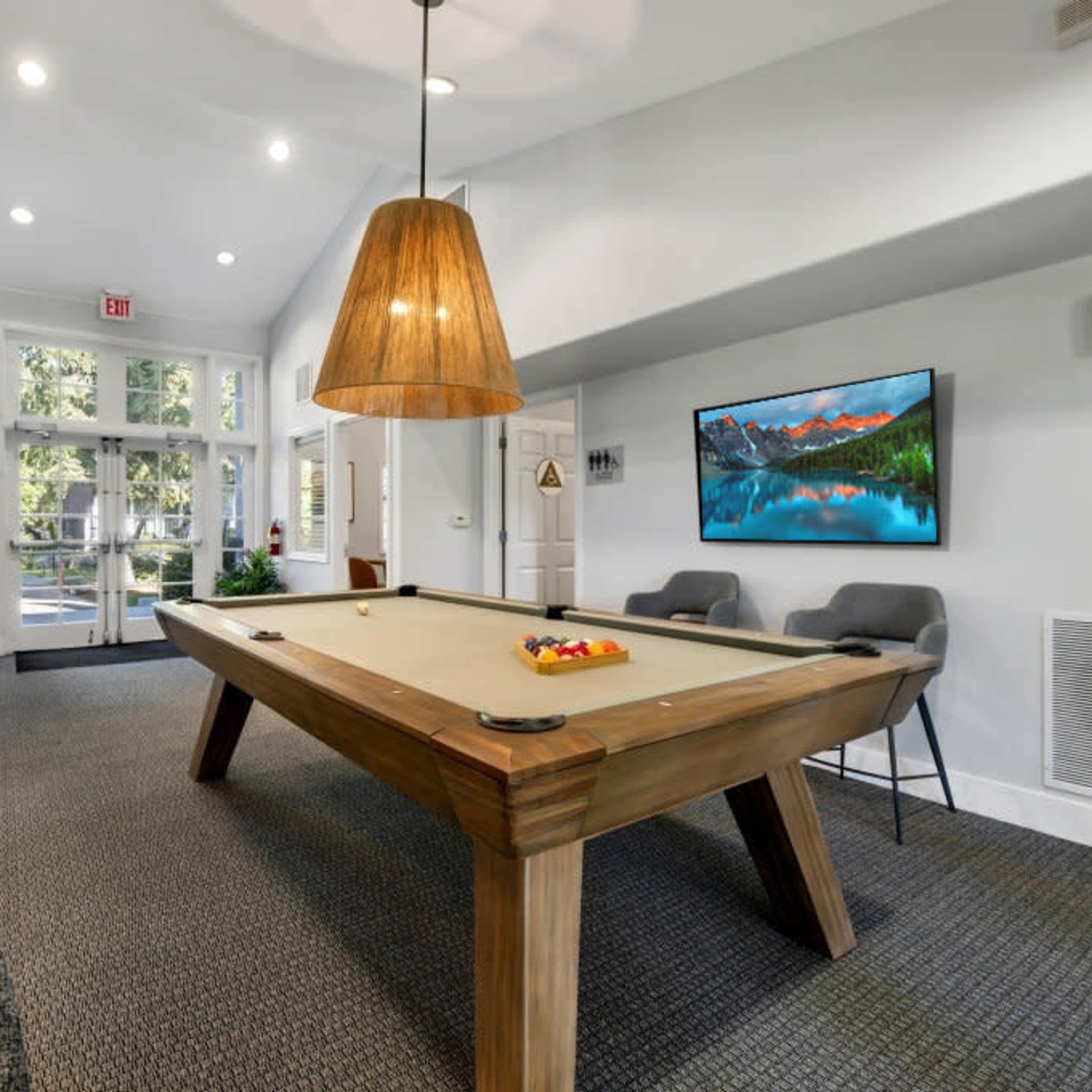 A spacious lobby features a wooden pool table under a large pendant light, with seating and a wall-mounted television in view.