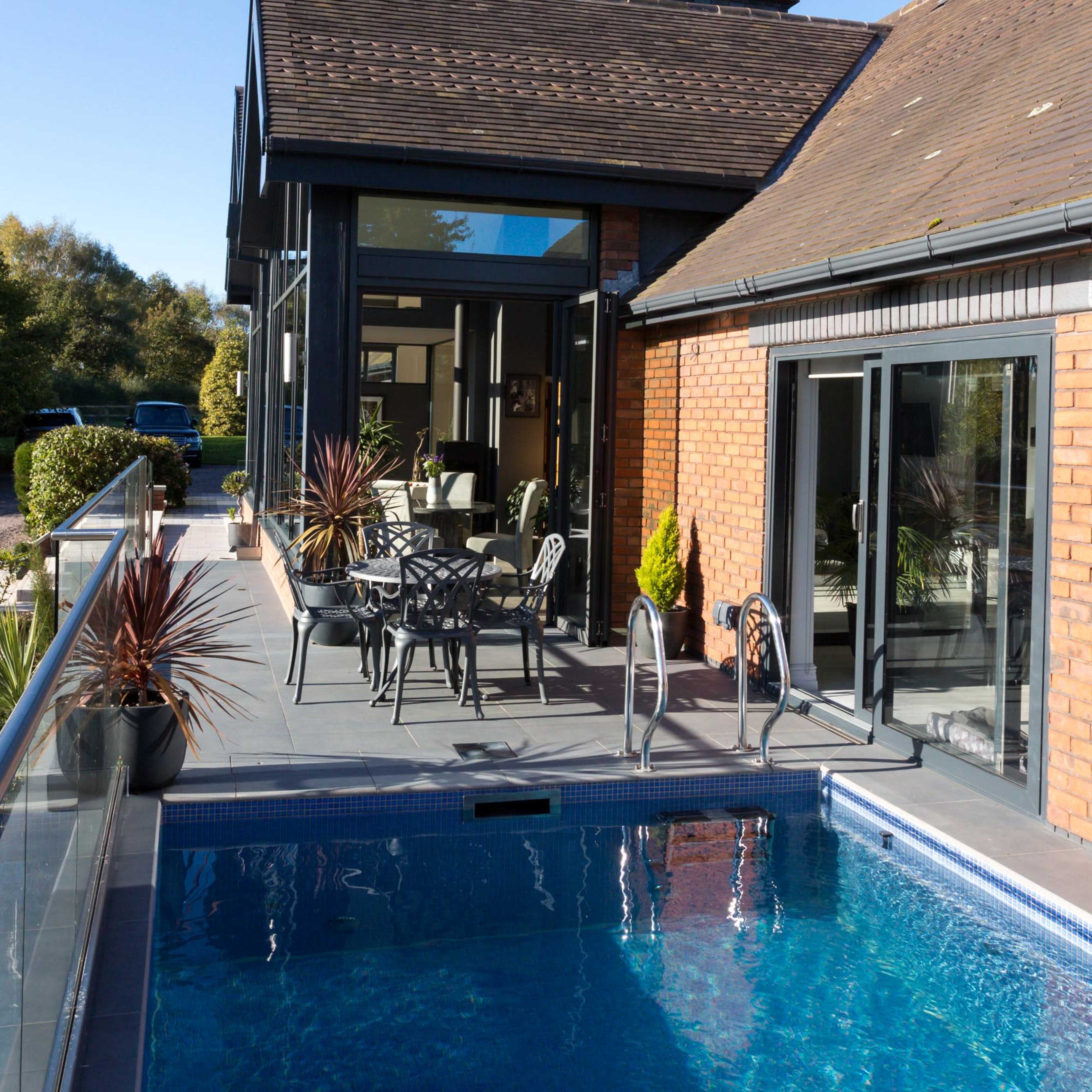 A modern house with a brick exterior features a swimming pool and a patio with outdoor furniture.